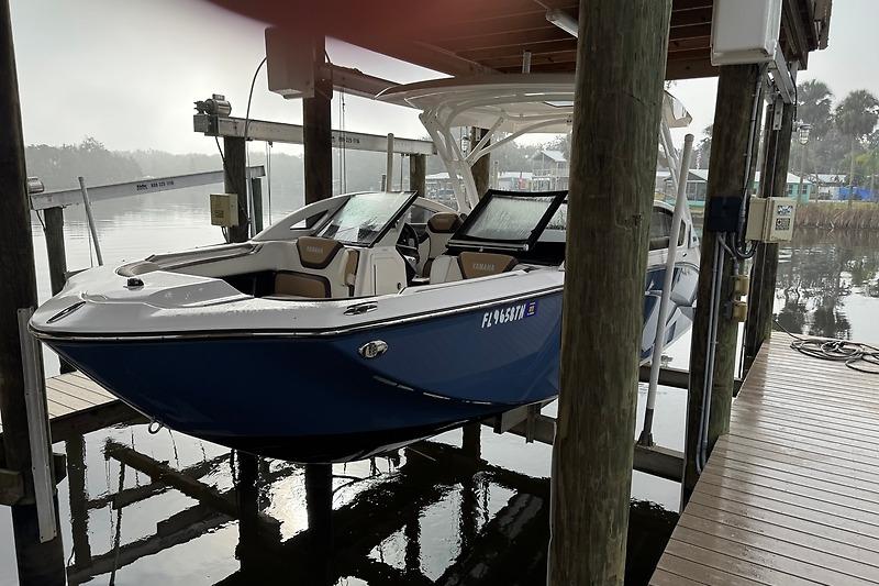2023 Yamaha 275SDX boat docked on a lift, blue hull, calm waters.