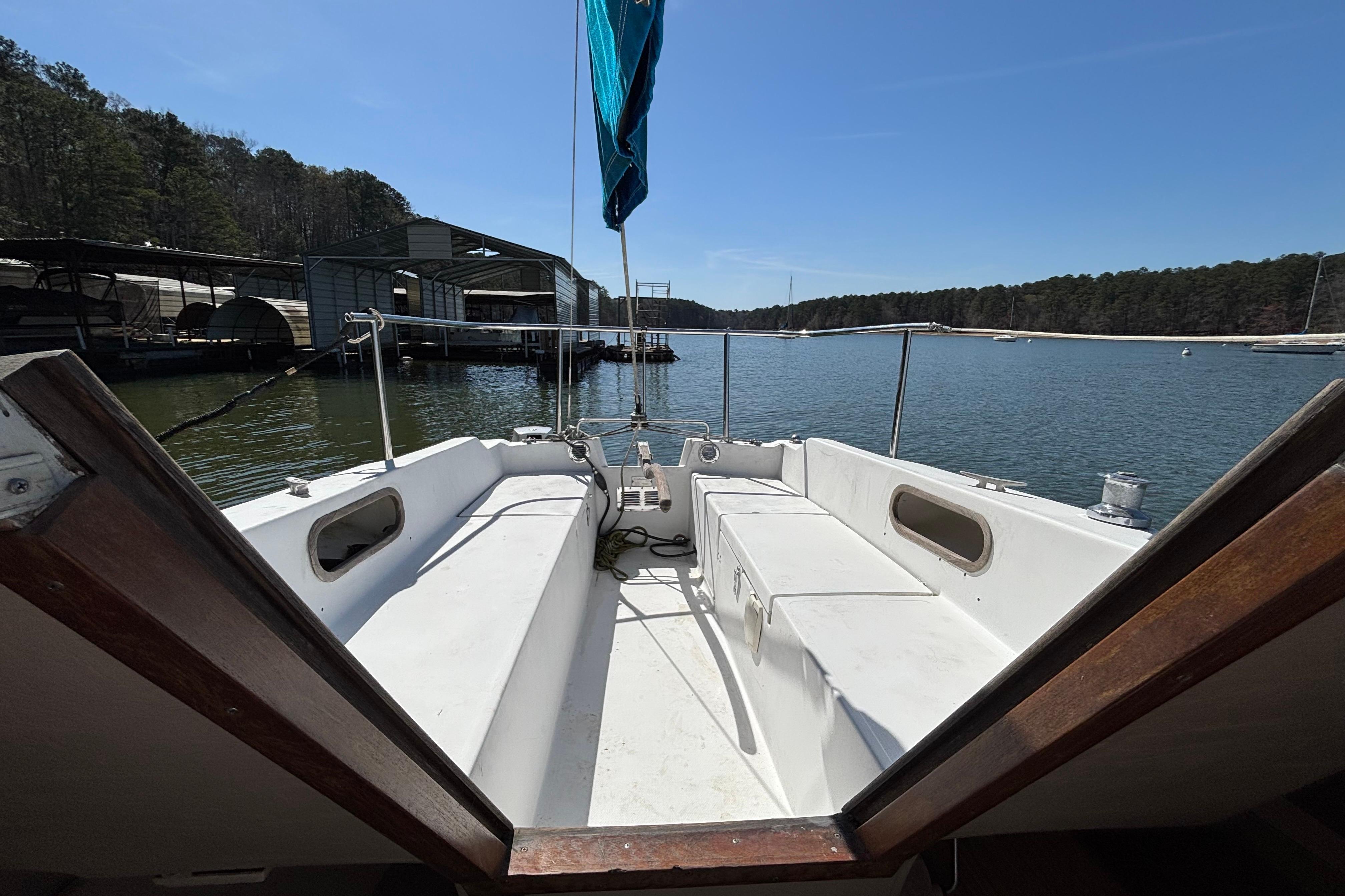 1983 Catalina 25 sailboat cockpit view, docked on a serene lake with forested shoreline.