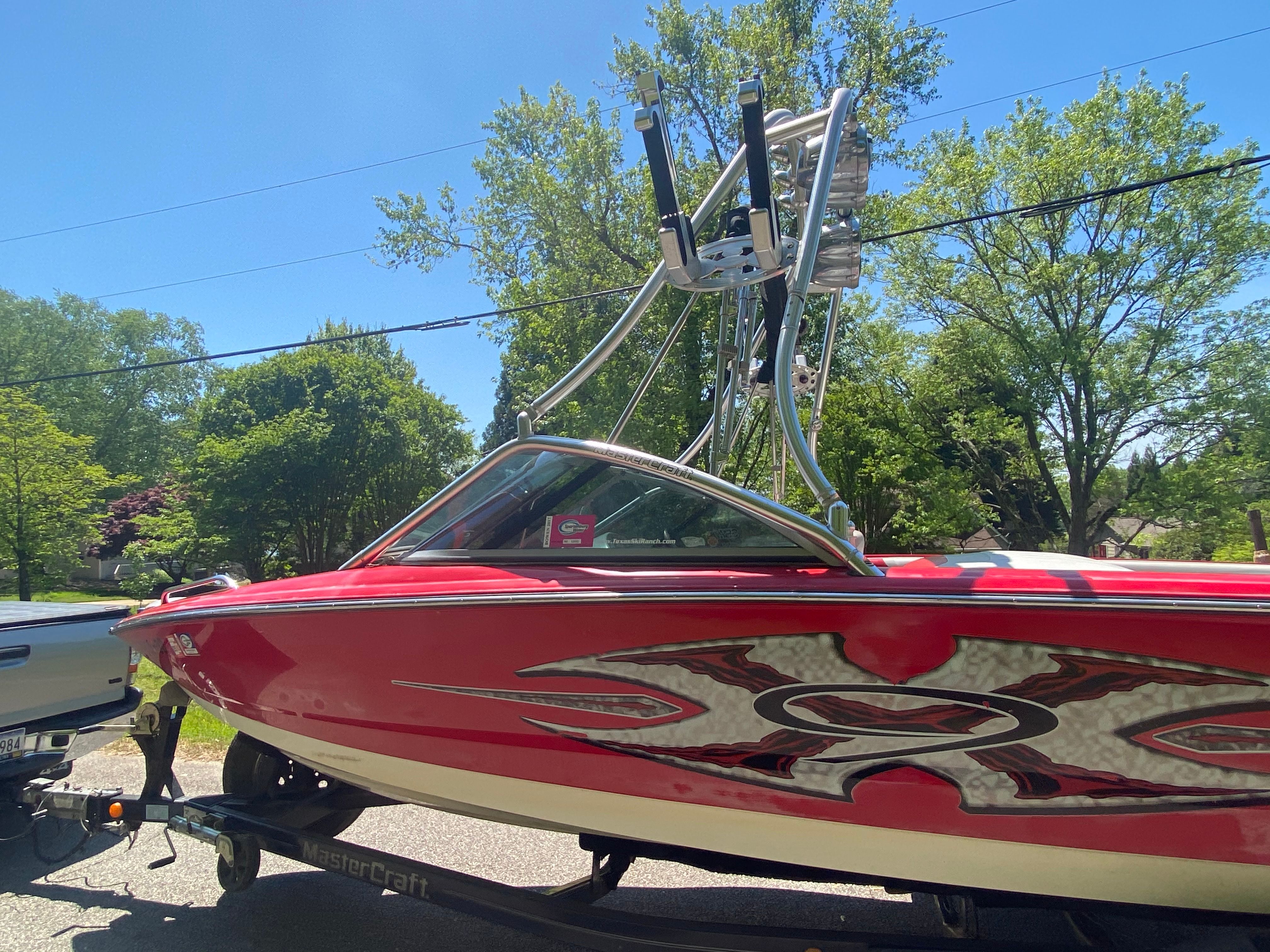 A red 2004 MasterCraft X-9 boat on a trailer, surrounded by trees.