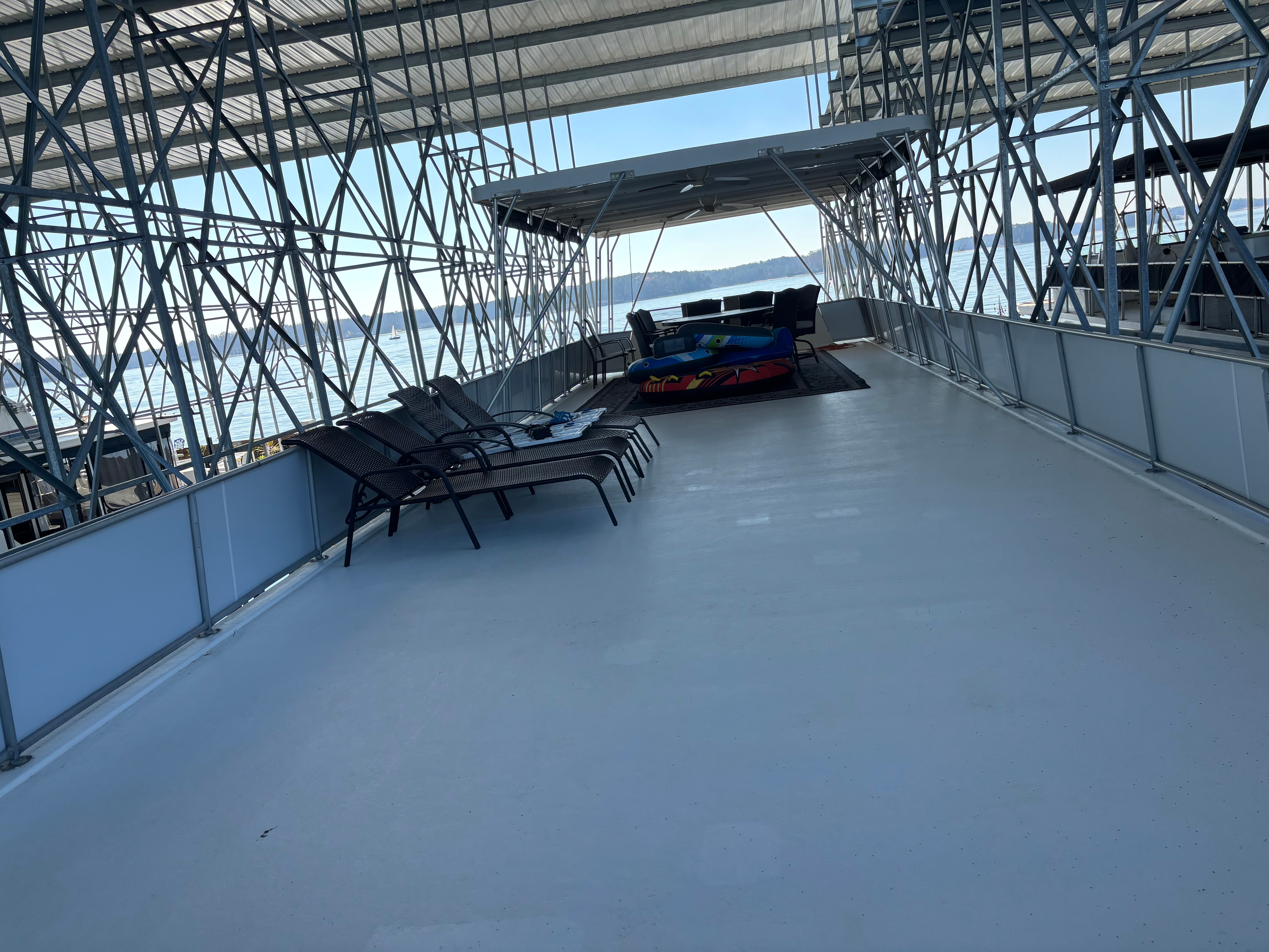 The image shows a houseboat deck with lounge chairs and a covered area.