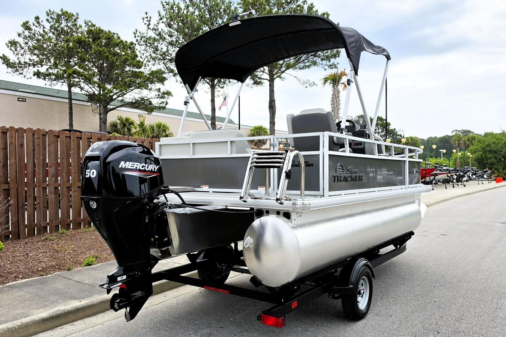 2026 Sun Tracker Bass Buggy 16 XL Select pontoon boat with Mercury 50 engine, parked outdoors.