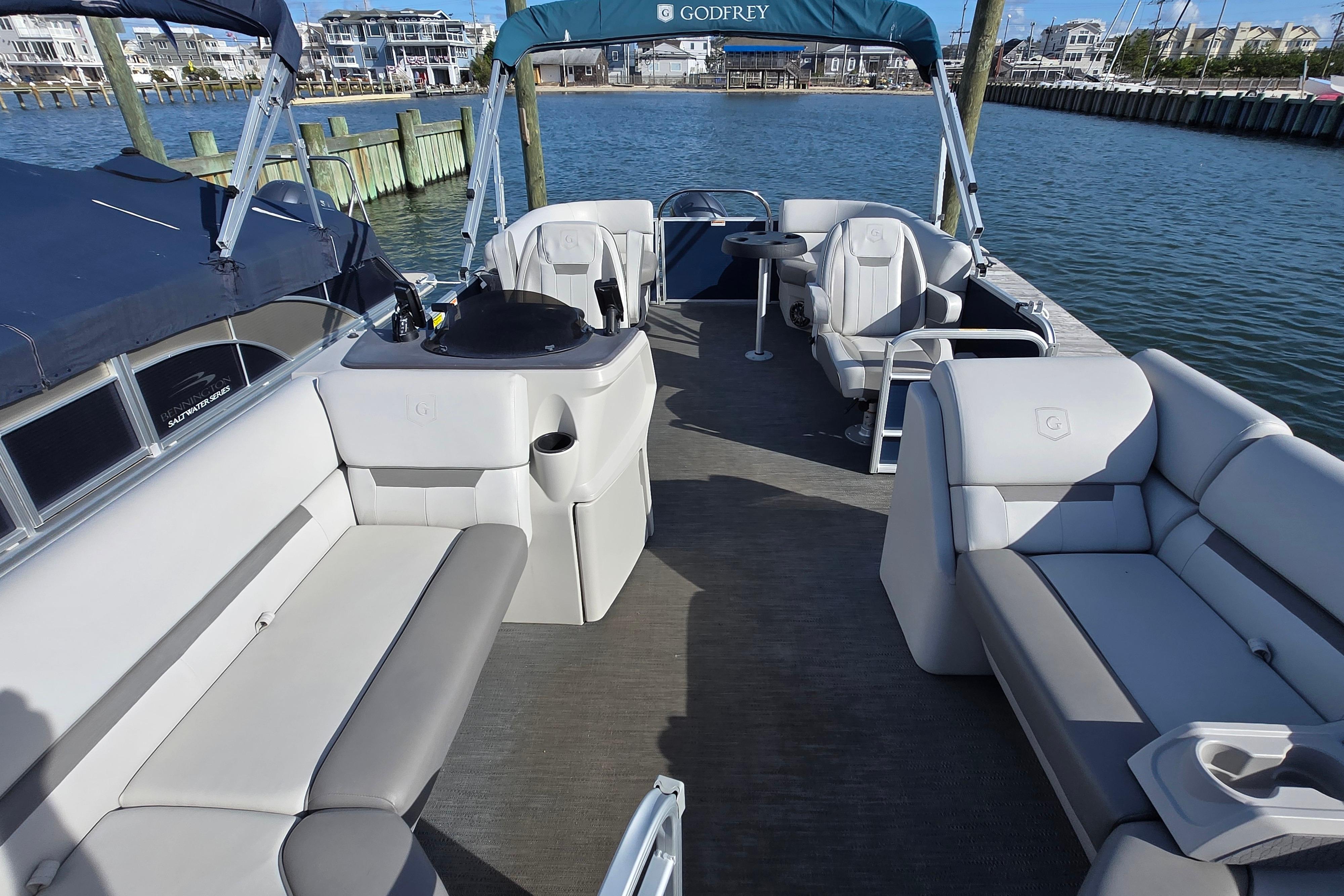 2023 Godfrey Sweetwater 2286 SBX pontoon boat interior with seating and helm, docked by the water.