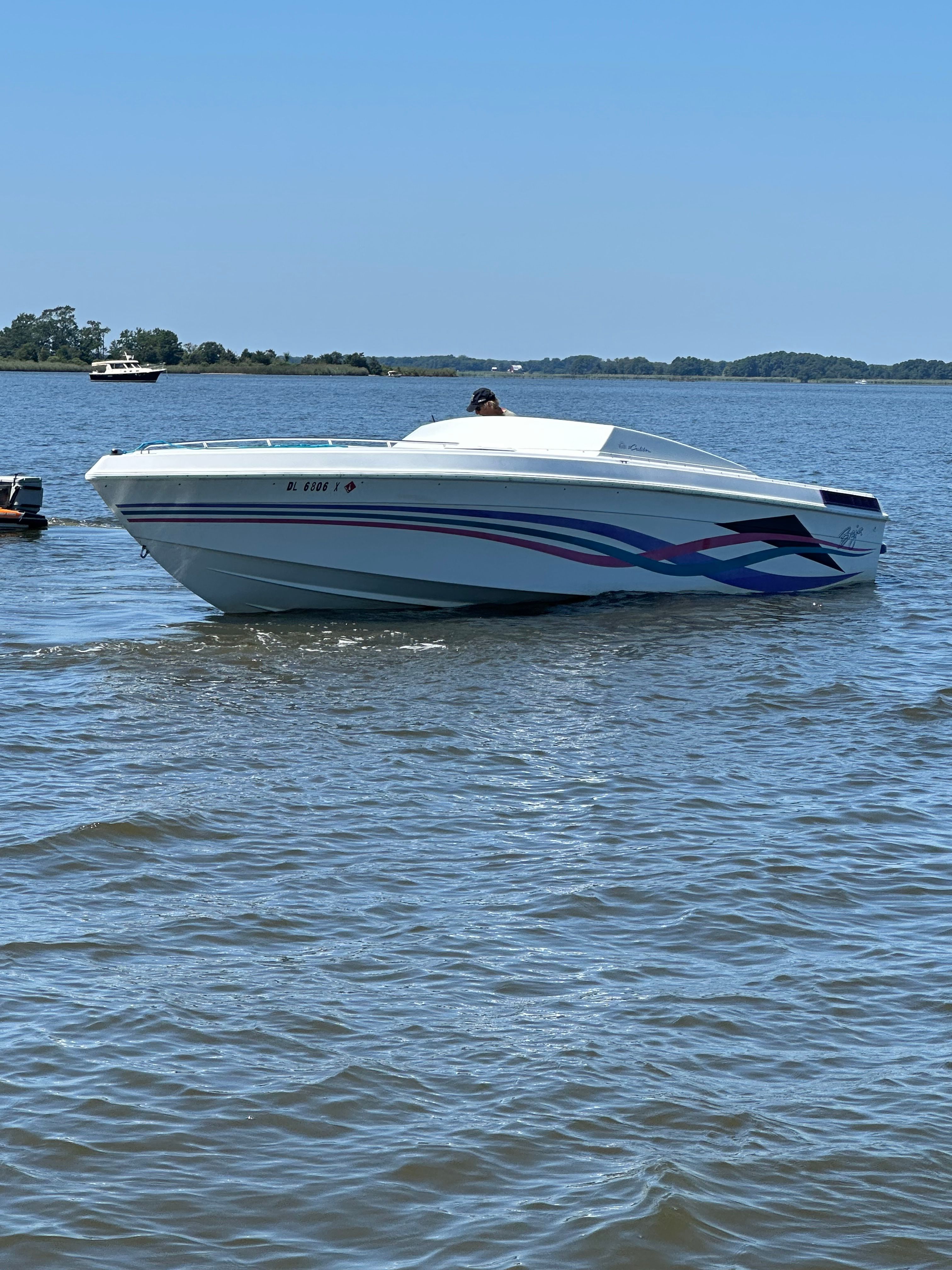 A 1995 Baja Caliber boat on the water with blue and red stripes.