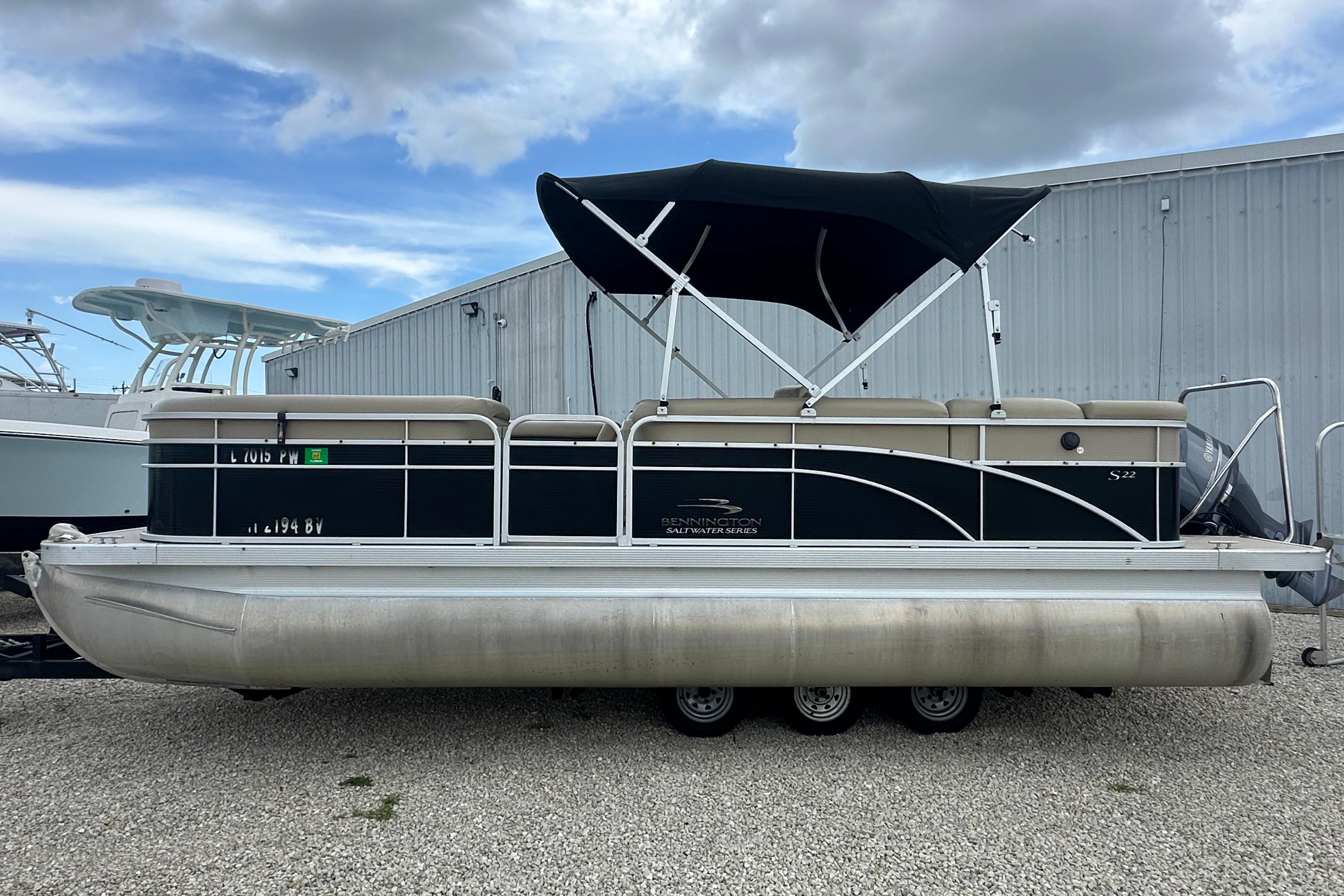 2014 Bennington S22 pontoon boat with canopy, parked on gravel, under cloudy sky.