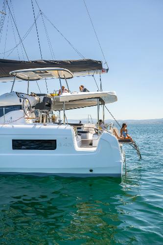 2025 Lagoon 43 catamaran sailing on clear blue waters, people relaxing onboard.