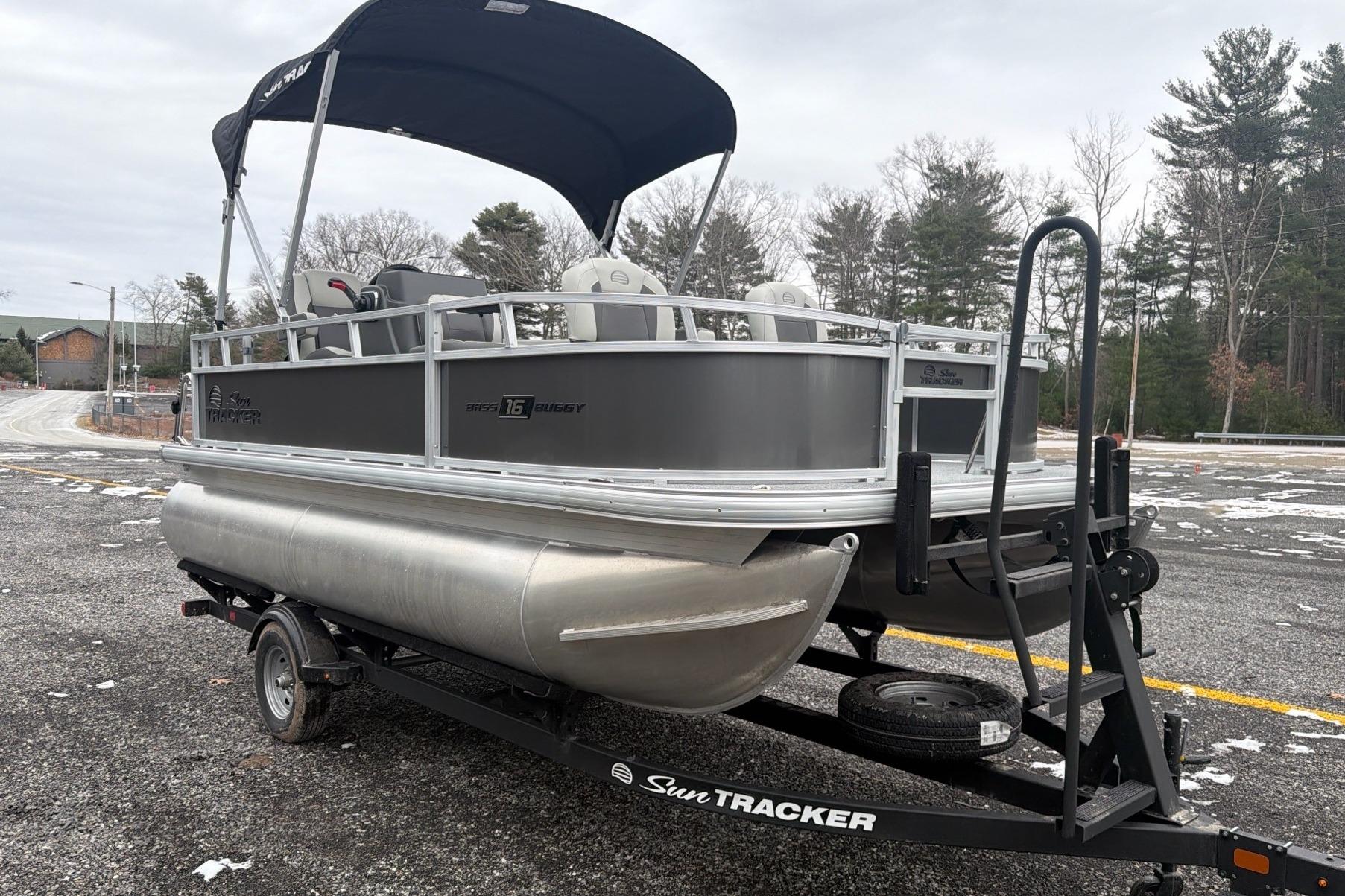 2026 Sun Tracker Bass Buggy 16 XL Select pontoon boat on trailer in parking lot.