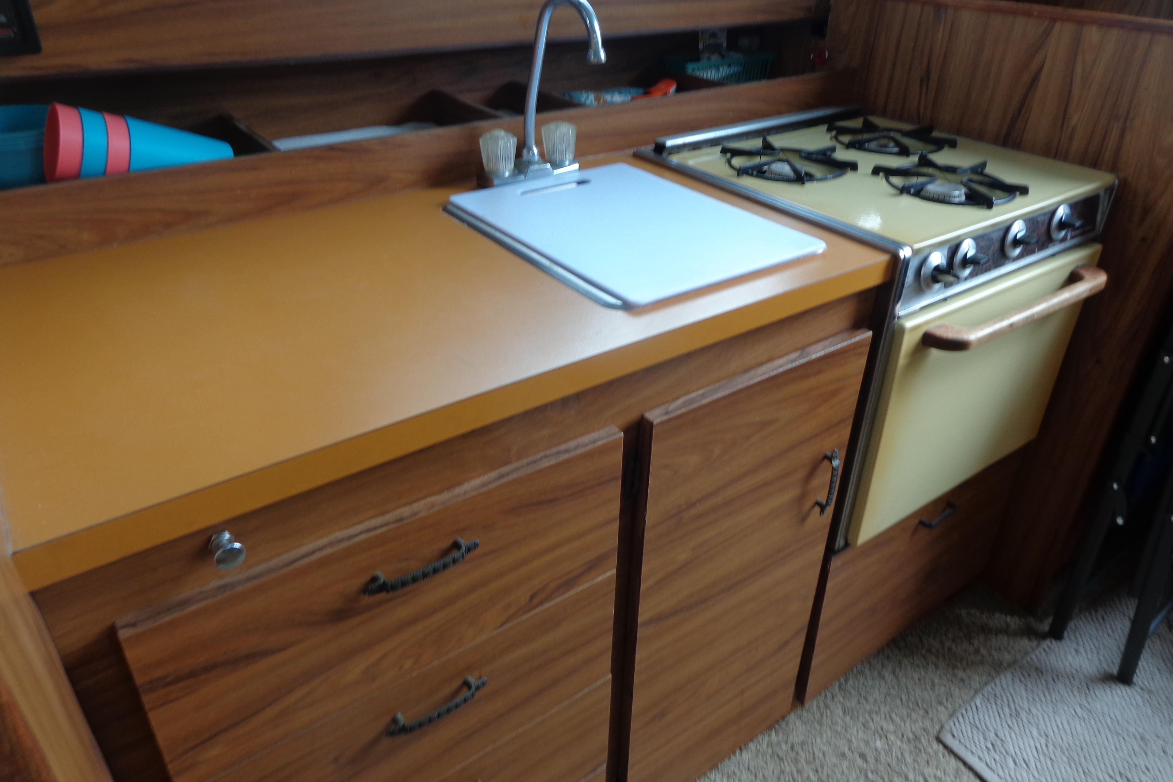 Vintage 1976 Tolly sedan kitchen with wood cabinets, yellow countertop, and retro stove.
