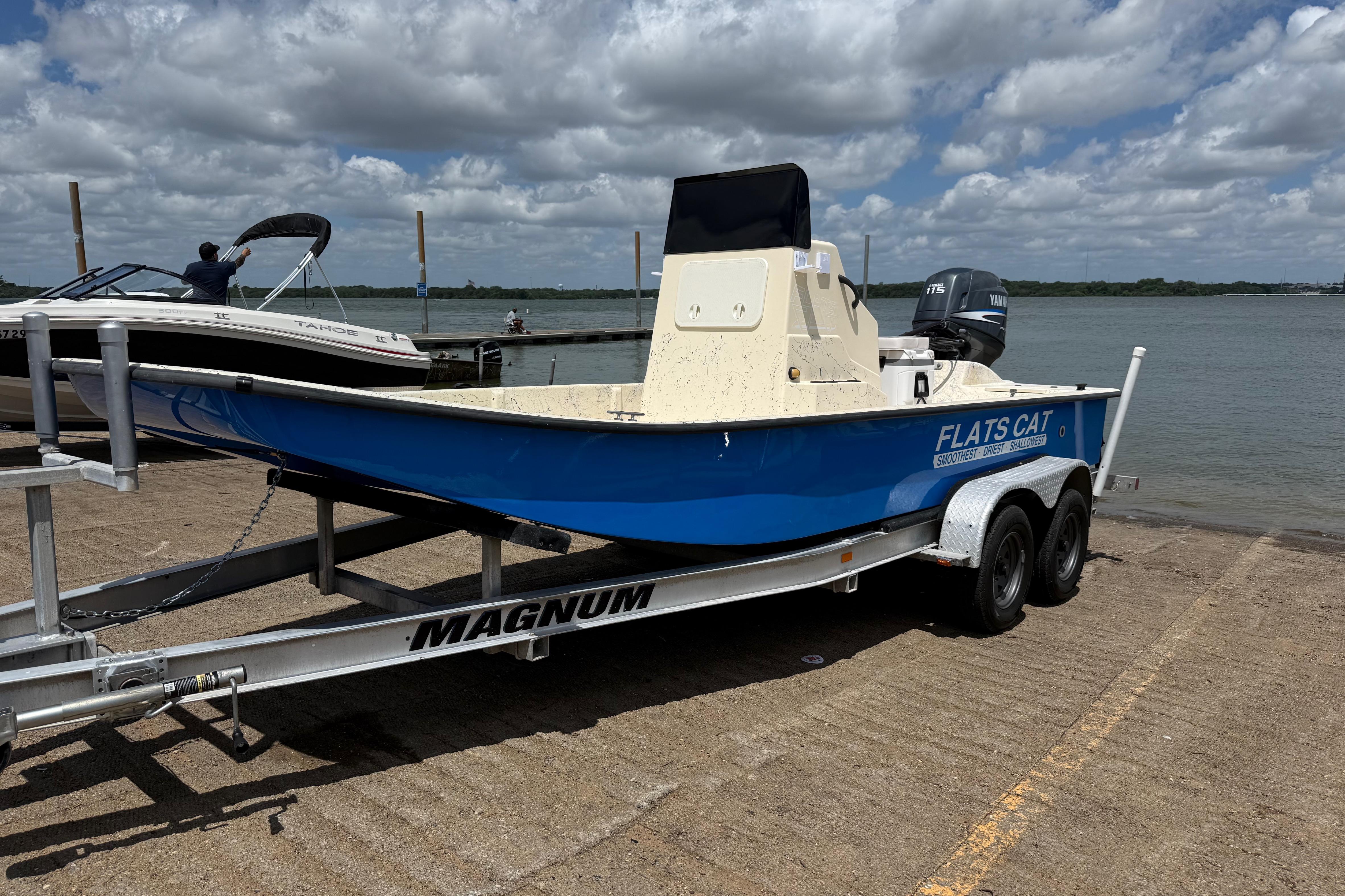 2007 Flats Cat 19 boat on trailer by lake under cloudy sky.