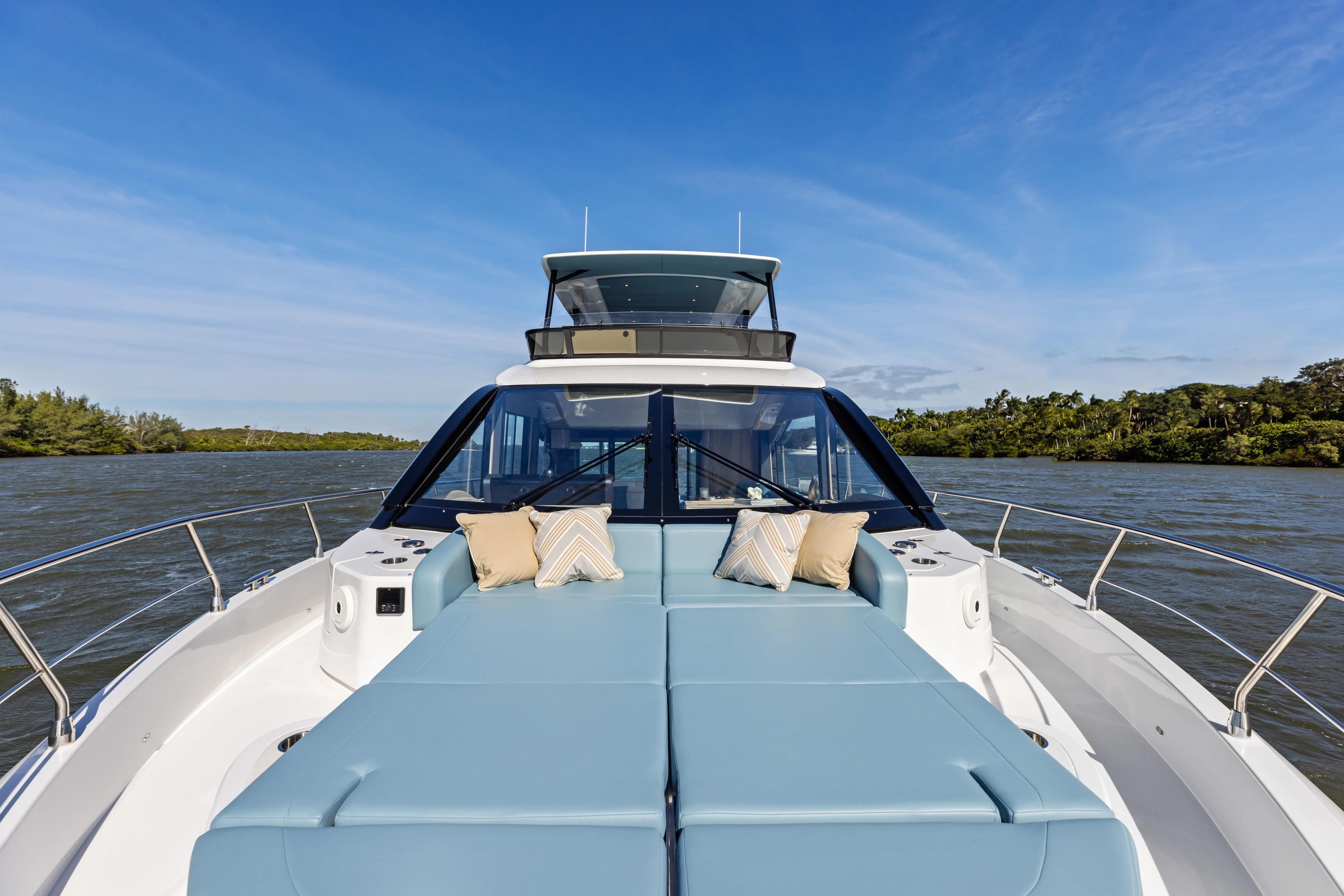 2026 Cruisers 50 Fly yacht with blue sunbeds on a serene river.
