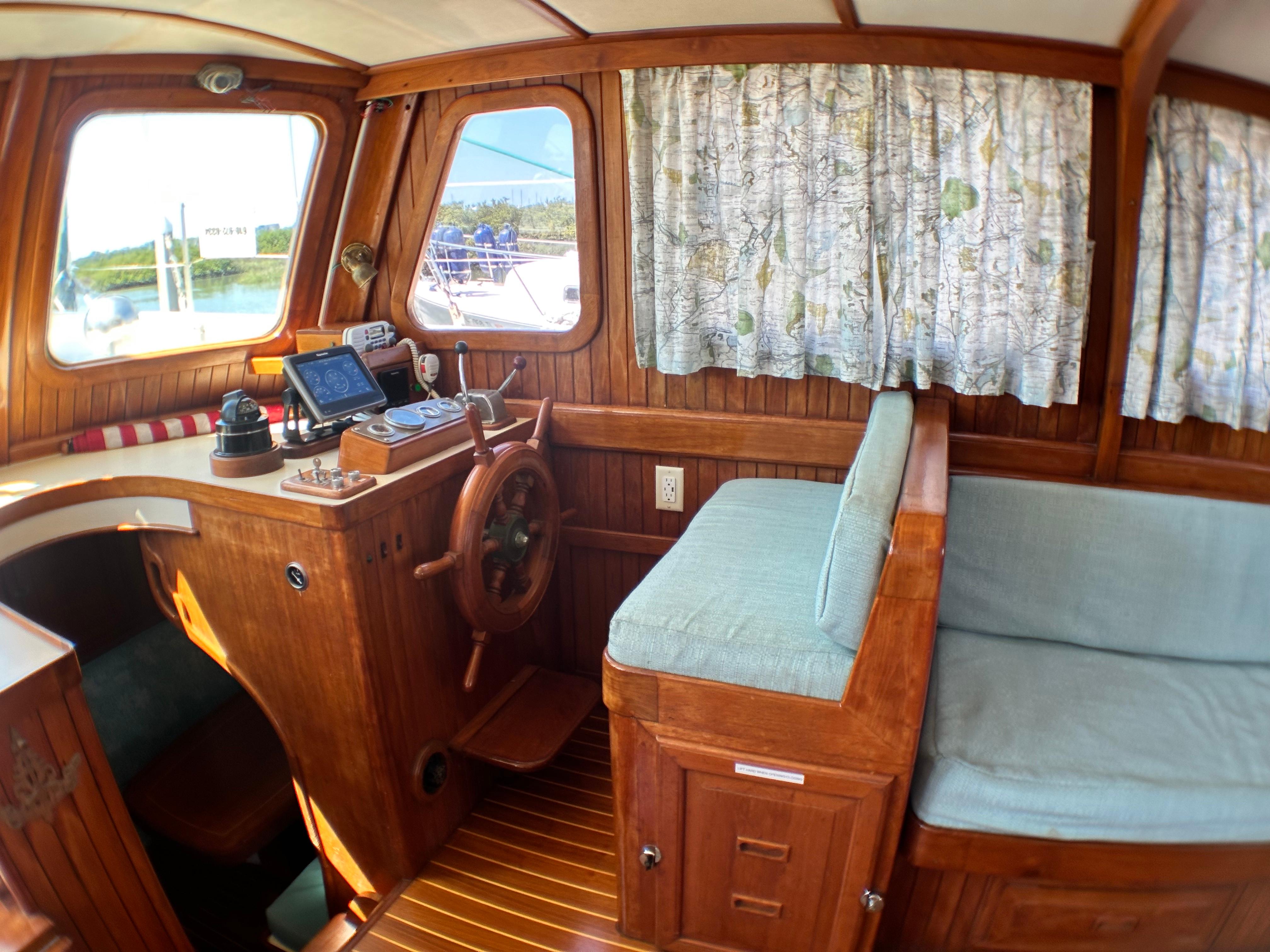 1981 Island Trader 46 interior with wooden helm, nautical decor, and cushioned seating.
