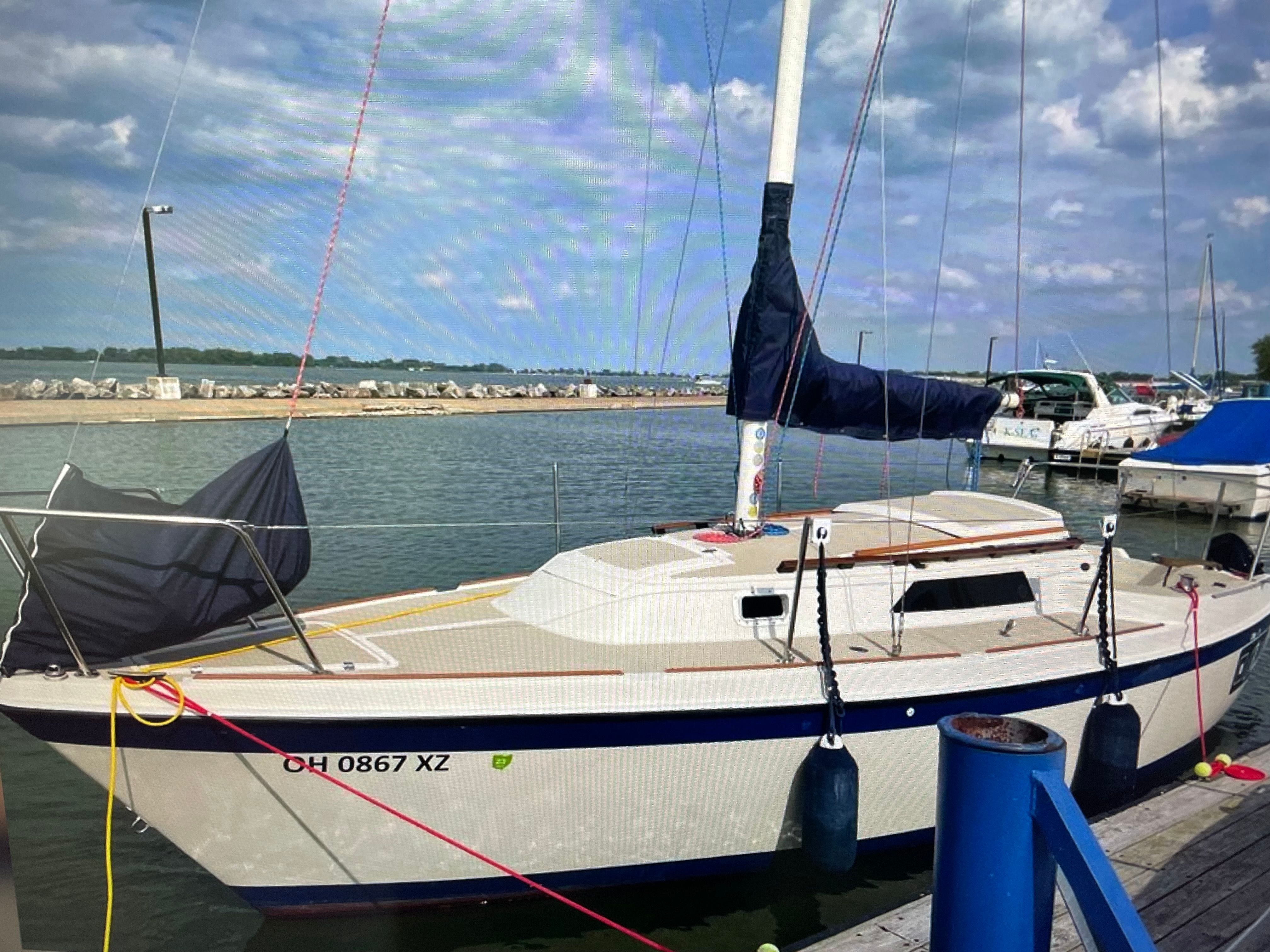 1984 O'Day 25 sailboat docked in harbor under cloudy sky.