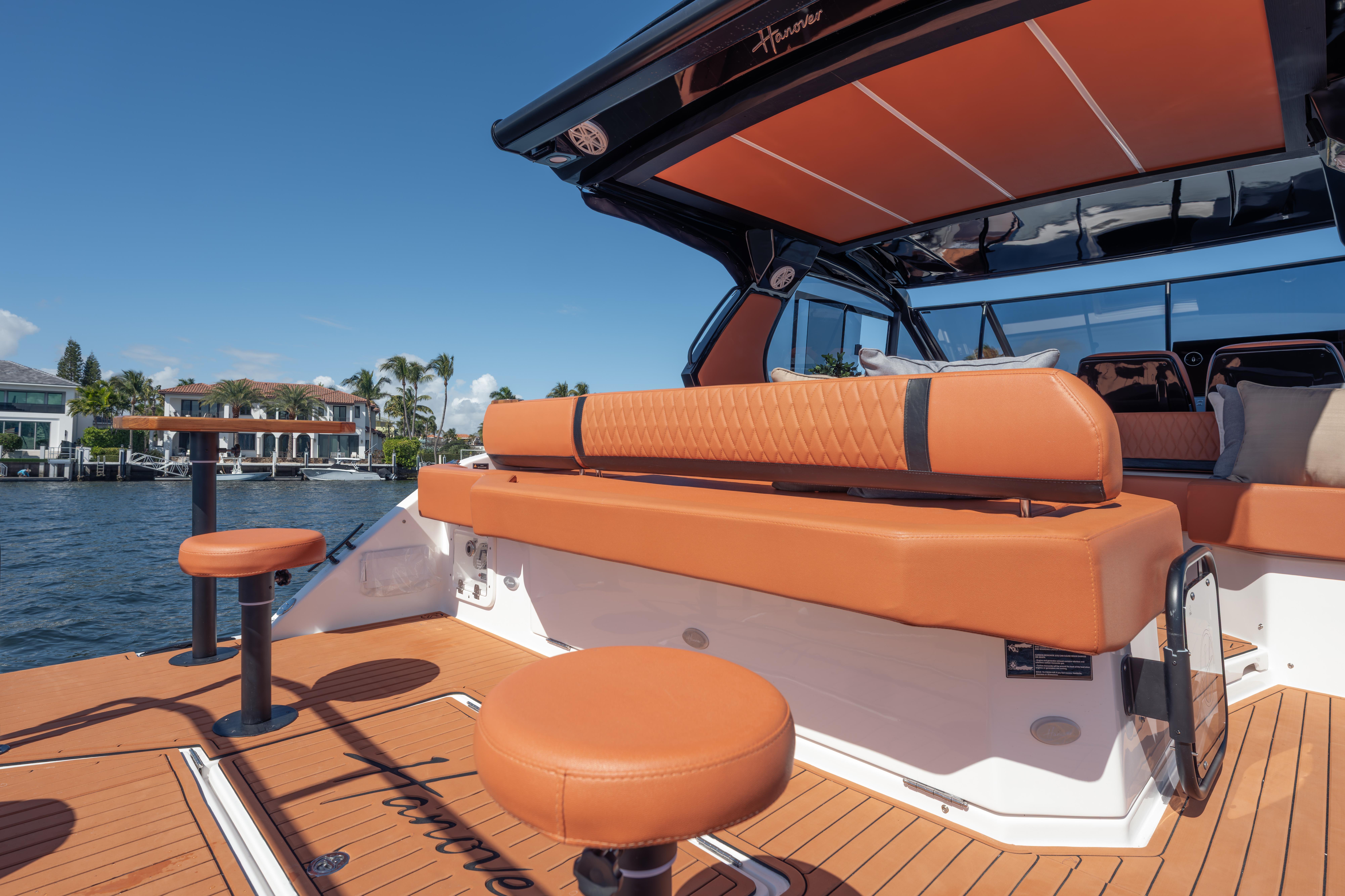 Luxurious 2026 Hanover 387 yacht interior with orange seating, docked by waterfront homes.