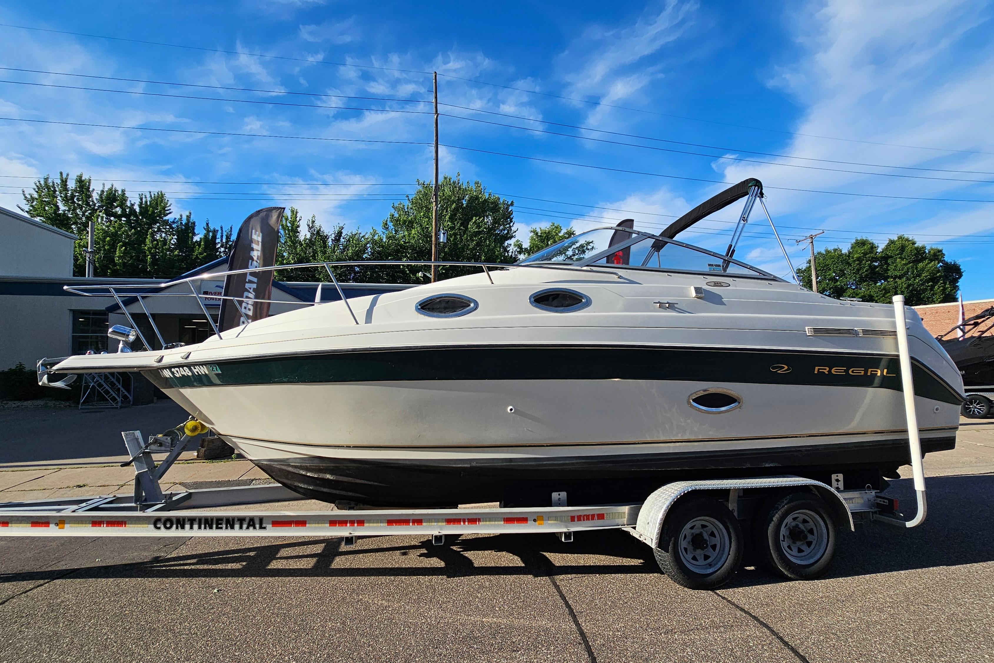 1999 Regal Commodore 258 boat on trailer, parked outdoors under a clear blue sky.