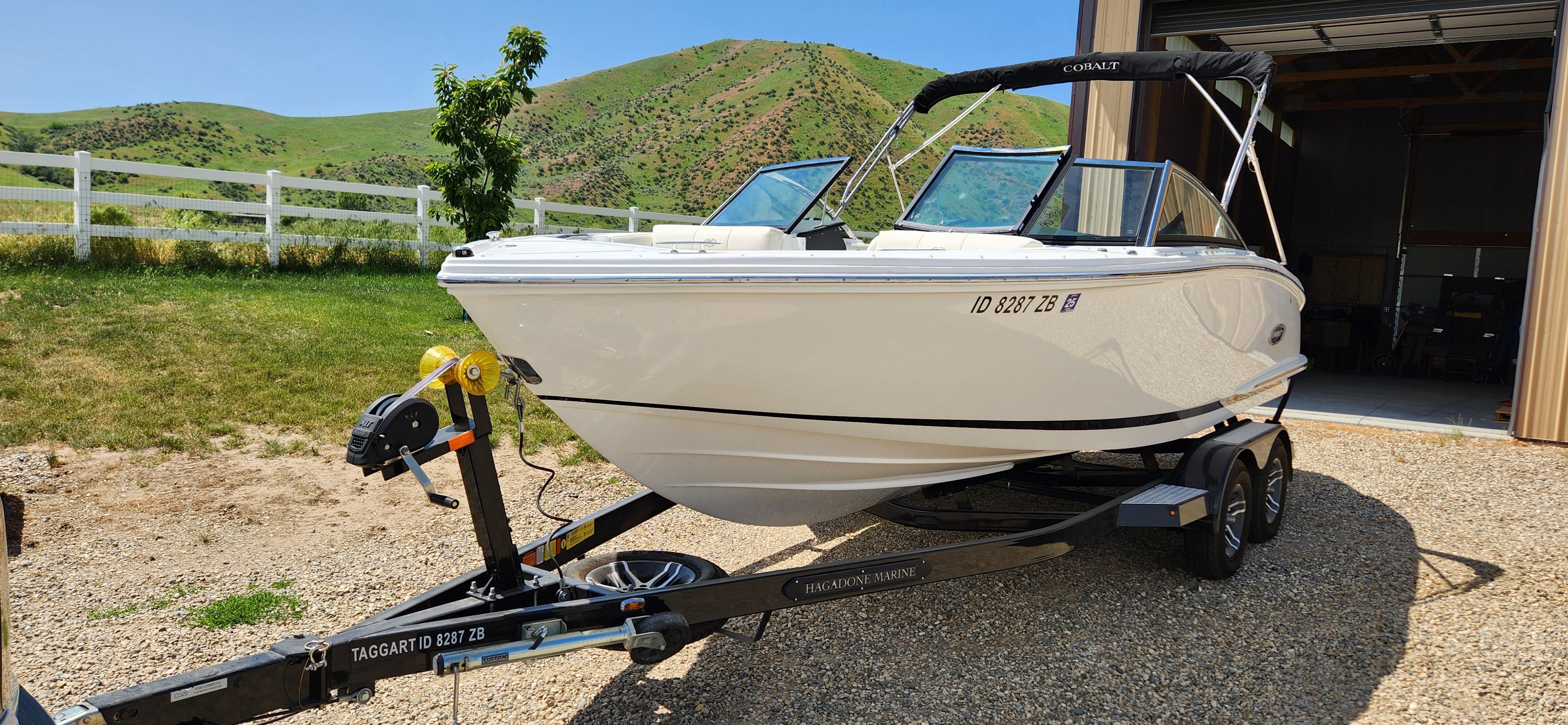 A white Cobalt CS22 boat on a trailer, parked in front of green hills.