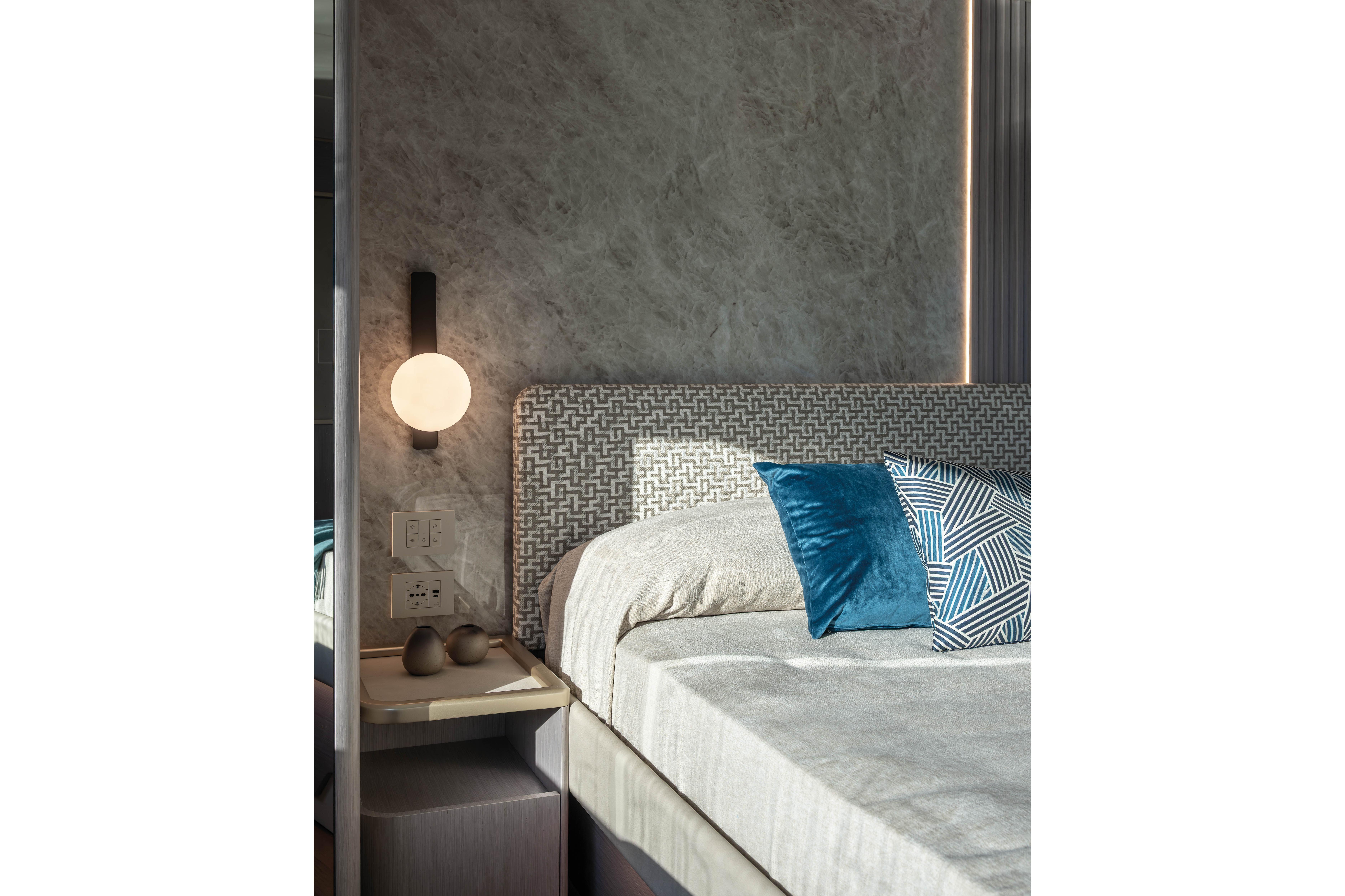 Modern bedroom with patterned headboard, blue pillows, and wall lamp.