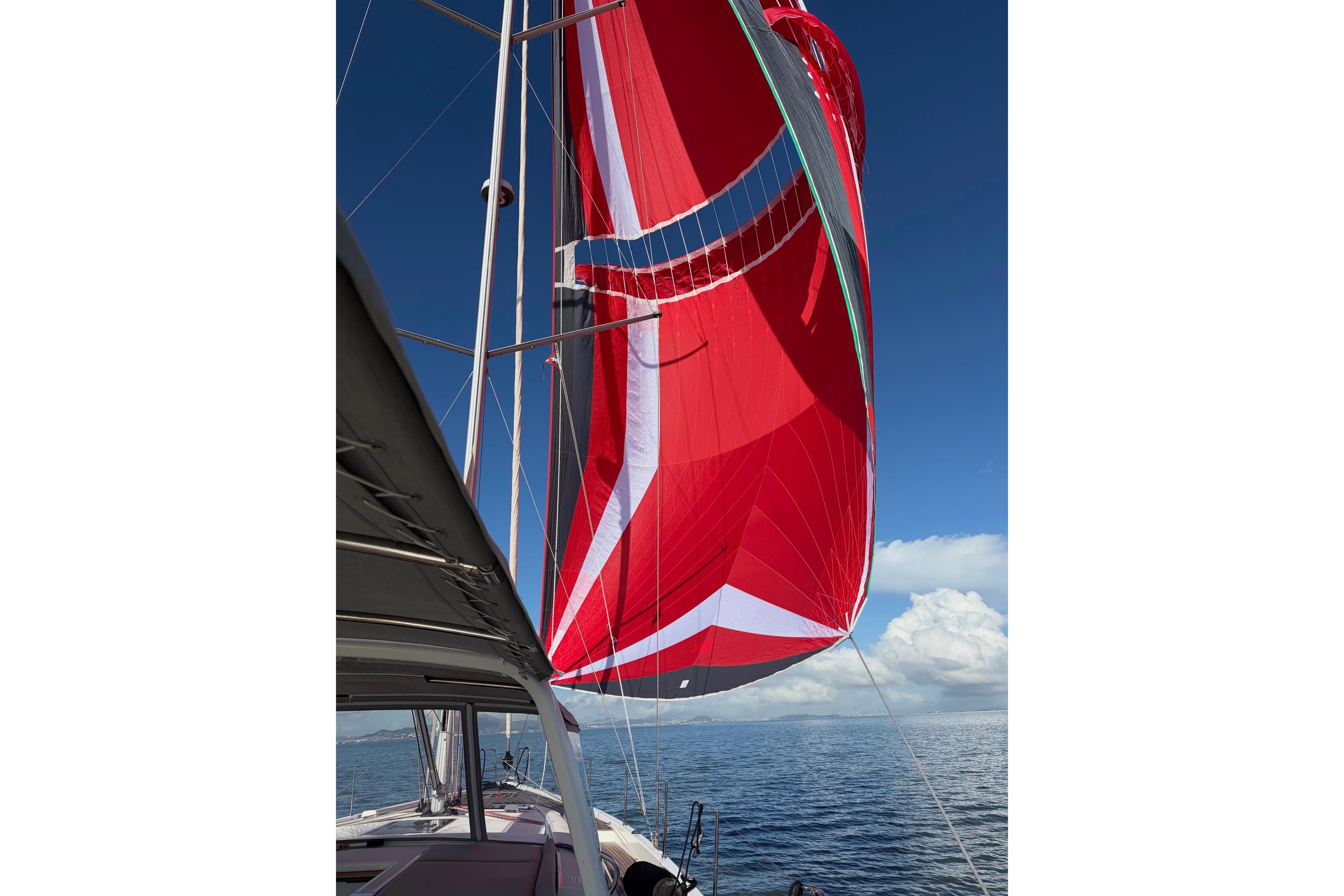 2022 Beneteau Oceanis Yacht 54 sailing with vibrant red spinnaker against blue sky.
