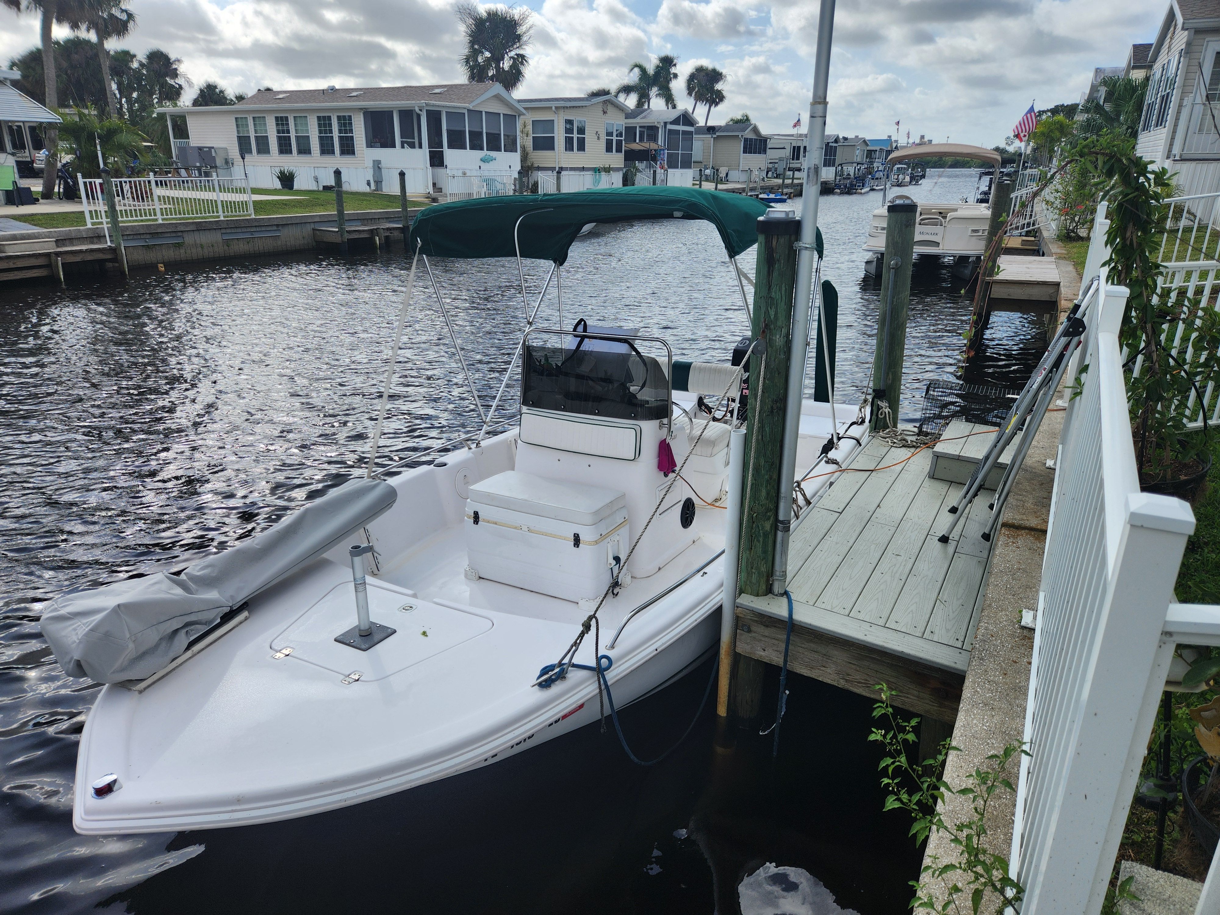 A white boat with a green sunshade docked in a residential area.