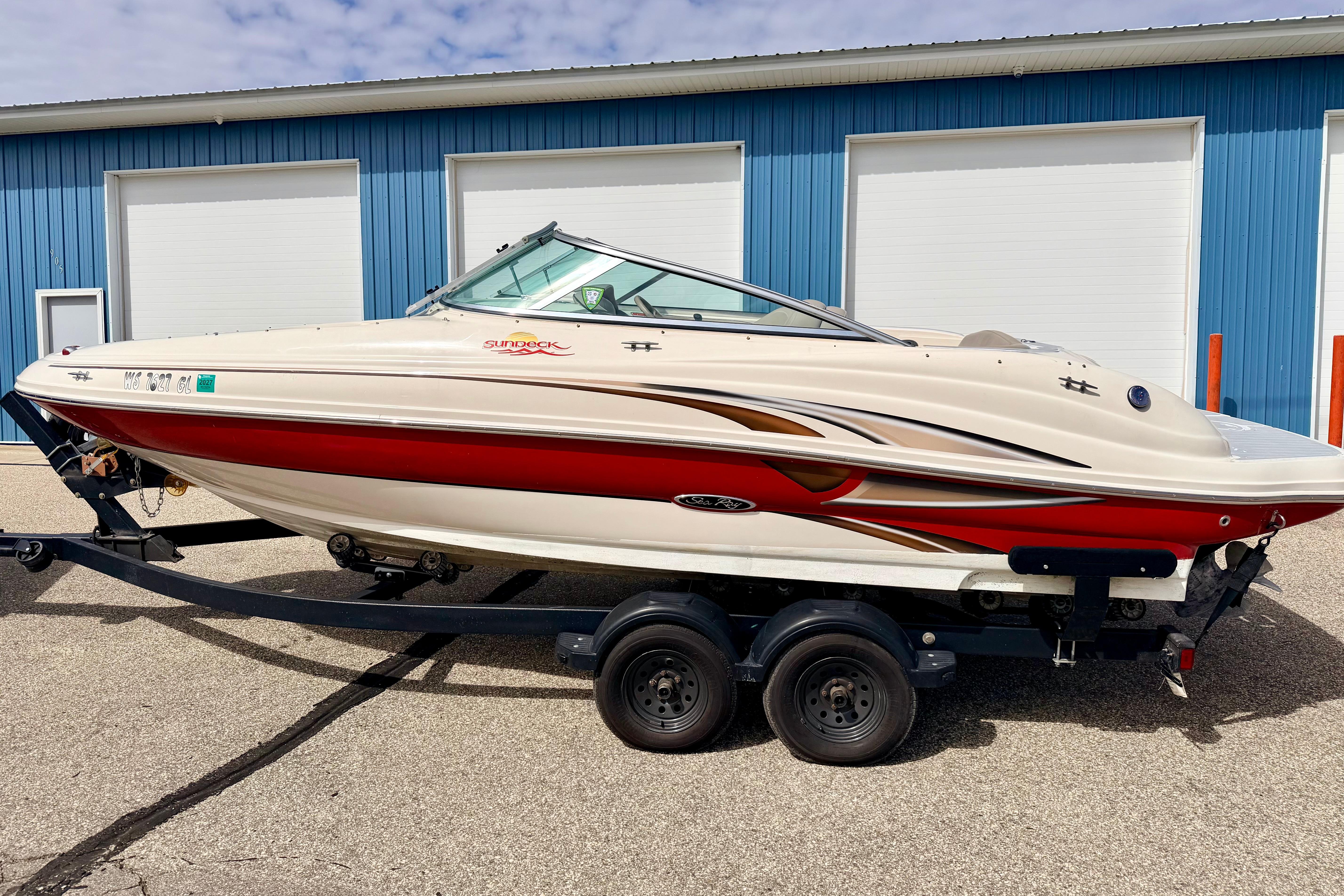 2003 Sea Ray 200 Sundeck boat on trailer, parked near blue building.