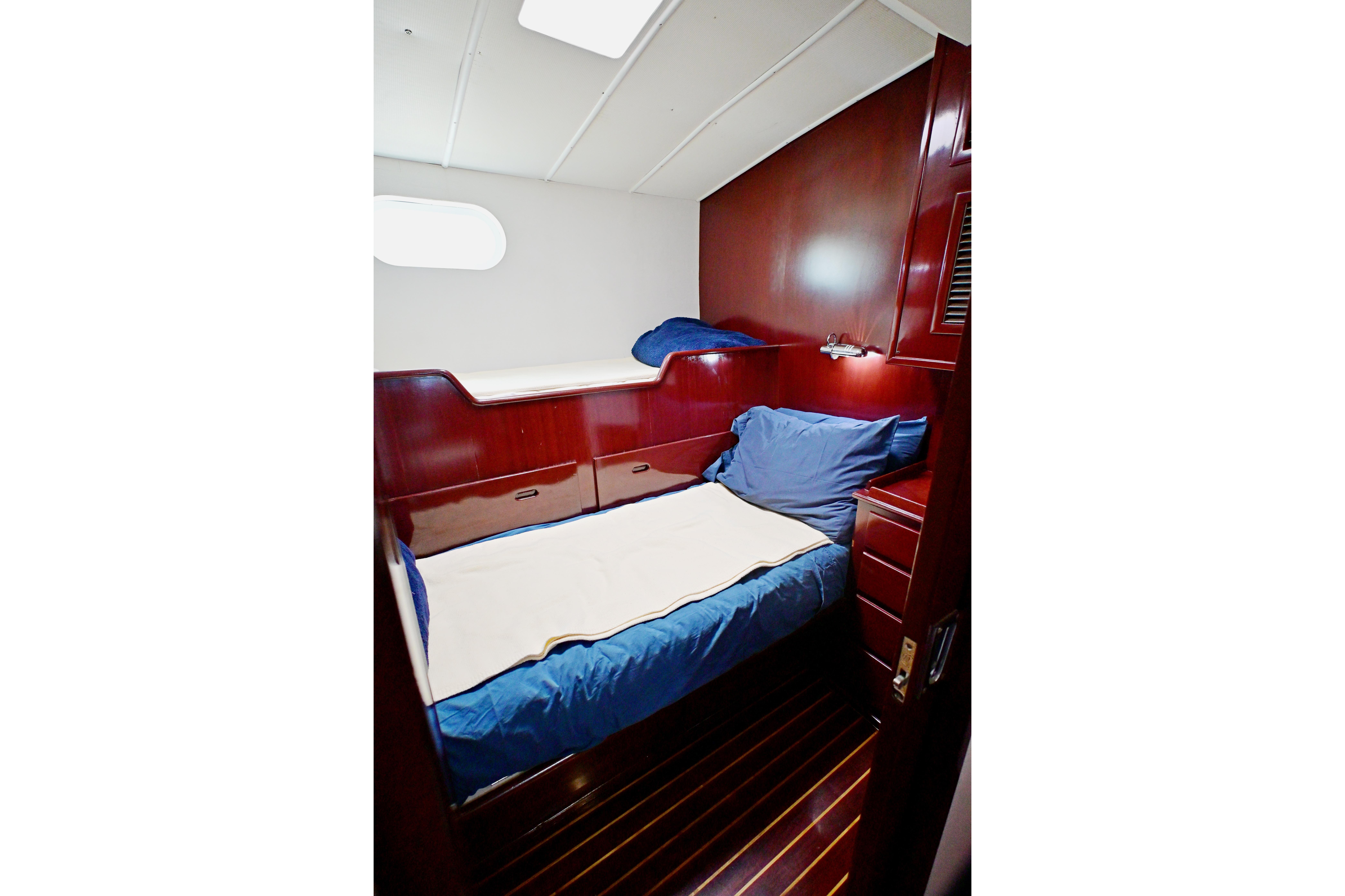 Cozy cabin interior of 1968 Abeking & Rasmussen Tripp 74 yacht with wooden finish and blue bedding.