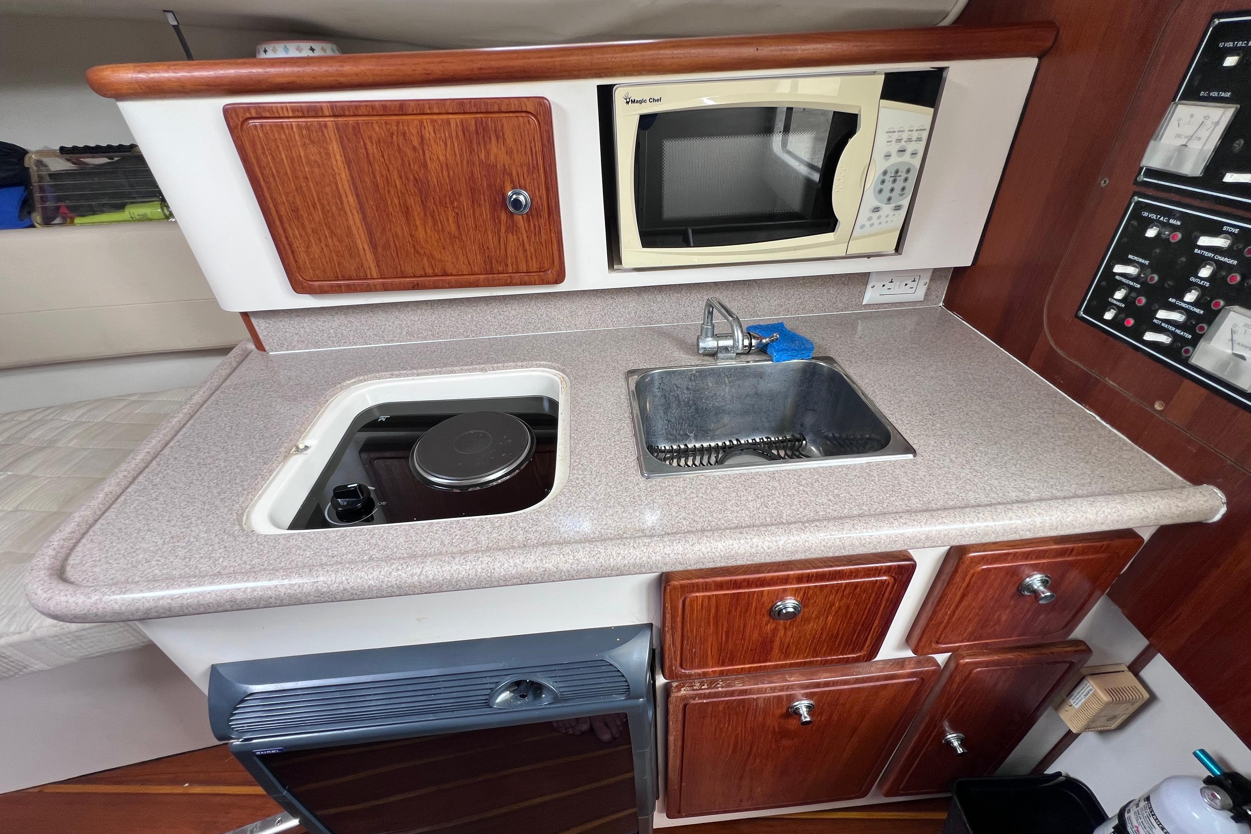 2005 Pursuit 3070 Offshore boat galley with sink, stove, microwave, and wooden cabinets.