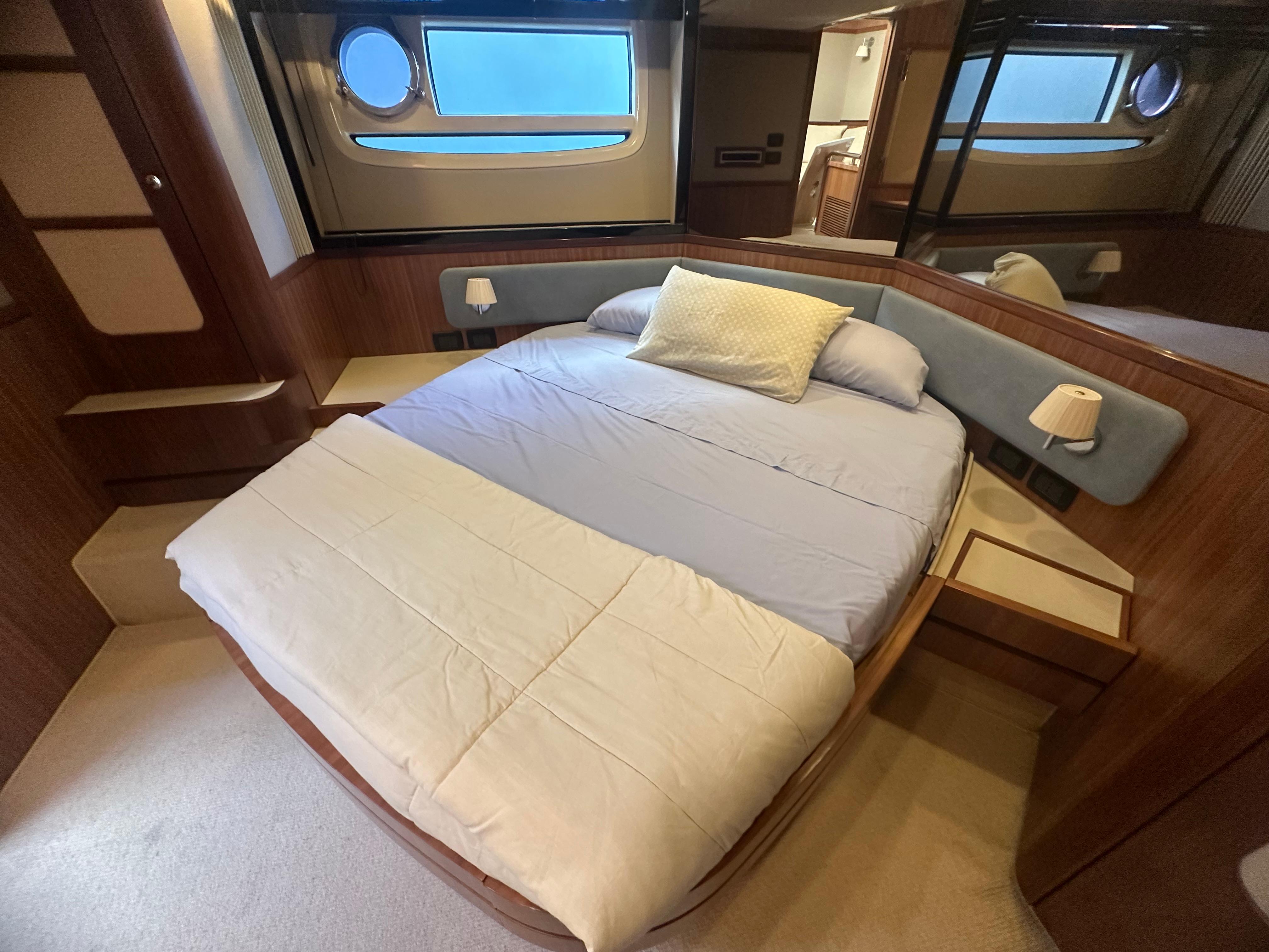 Luxurious bedroom interior of 2014 Azimut Magellano 50 yacht with cozy bed and porthole view.