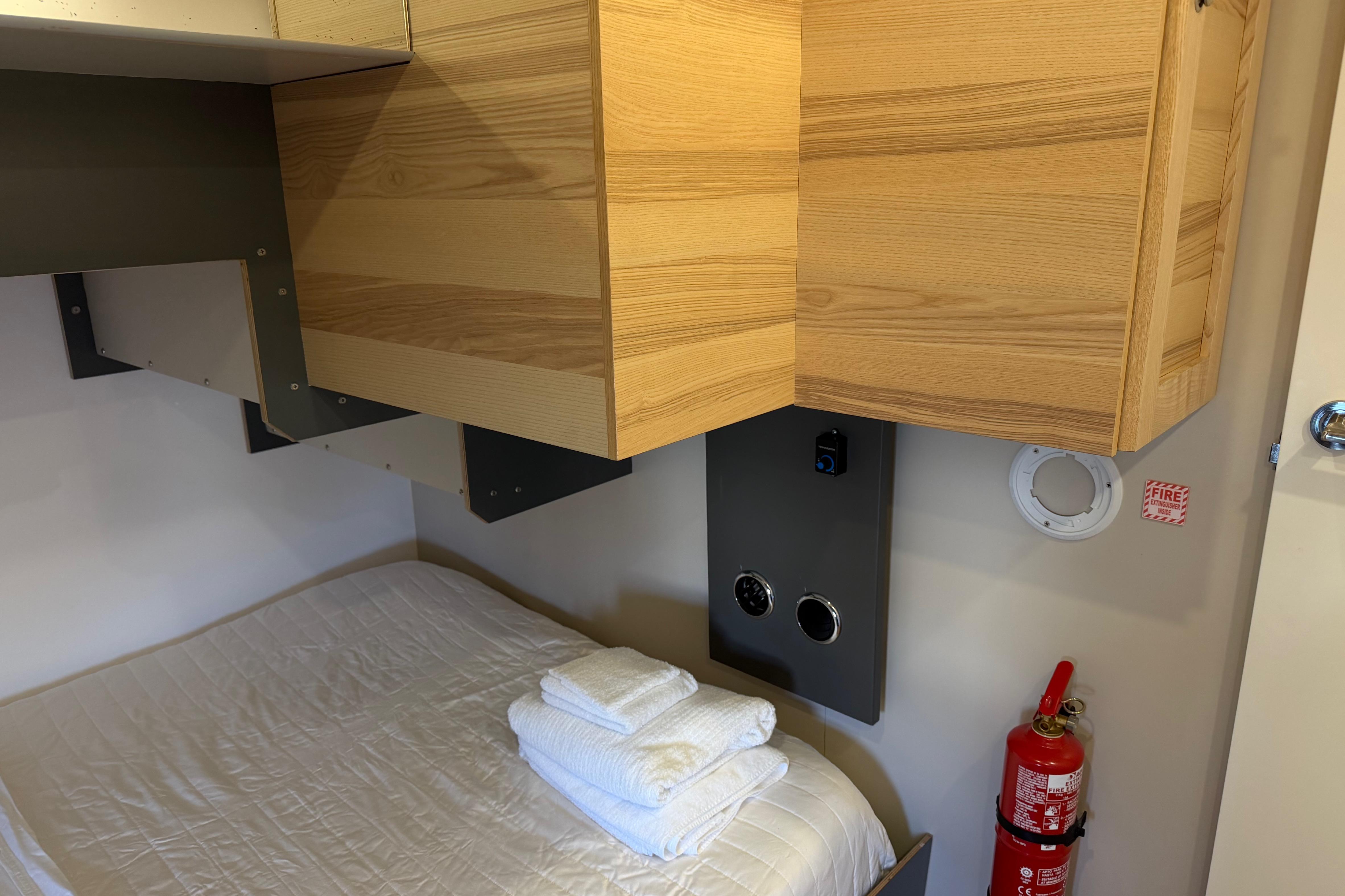 Compact cabin interior of 2022 Navisyo NV.08 with bed, wooden cabinets, and fire extinguisher.