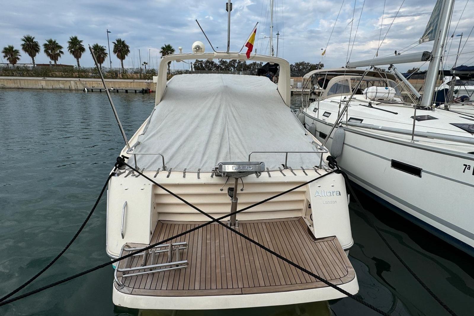 1989 Riva 43' Tropicana yacht docked, covered, with wooden deck and nearby sailboats.