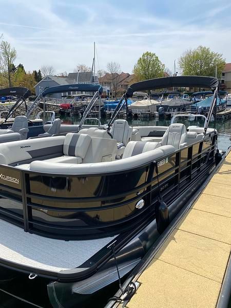 A sleek pontoon boat with gray seating, docked in a calm marina.