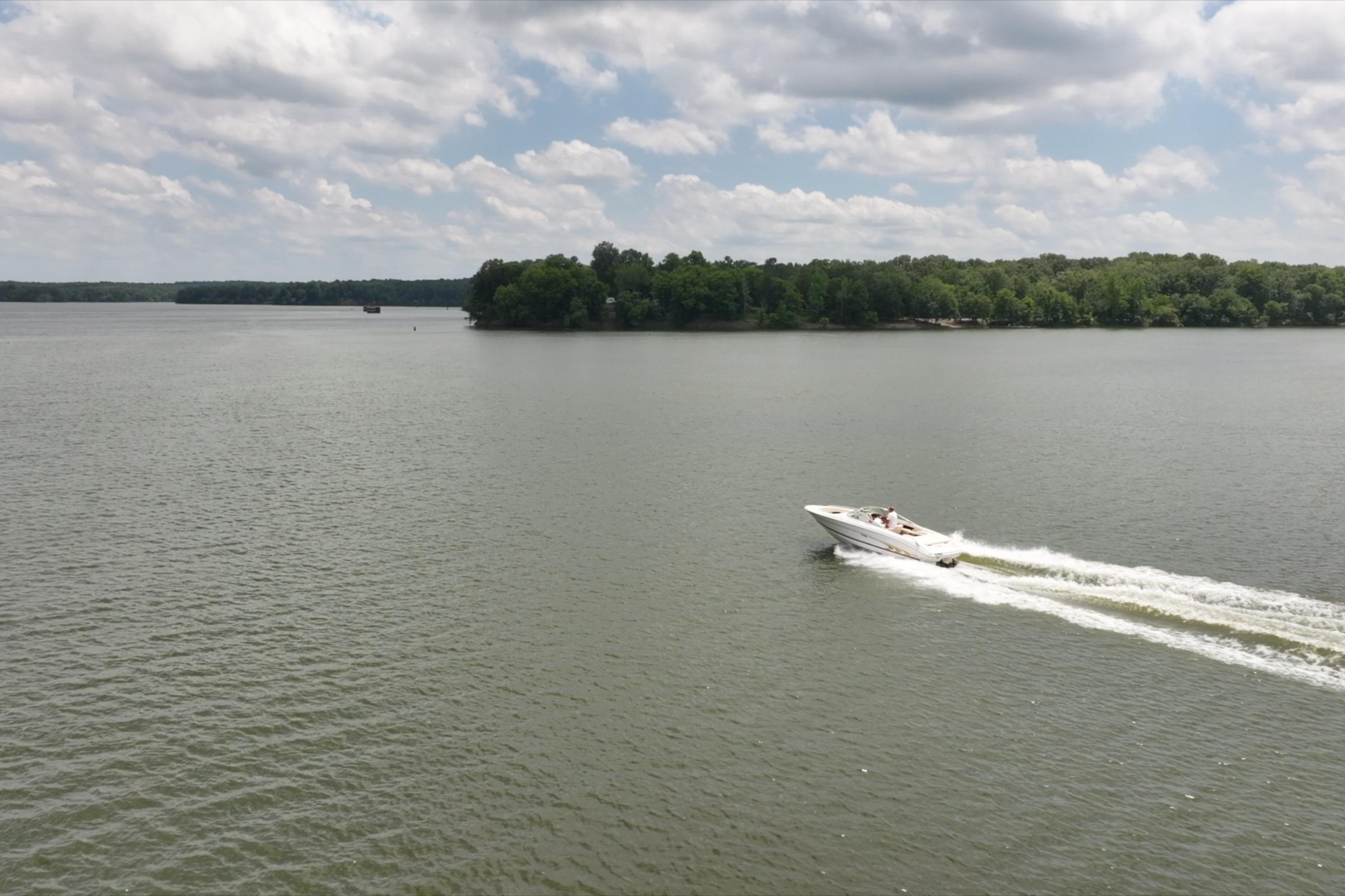 A 1997 Sea Ray 230 Signature boat cruising on a calm lake under a cloudy sky.