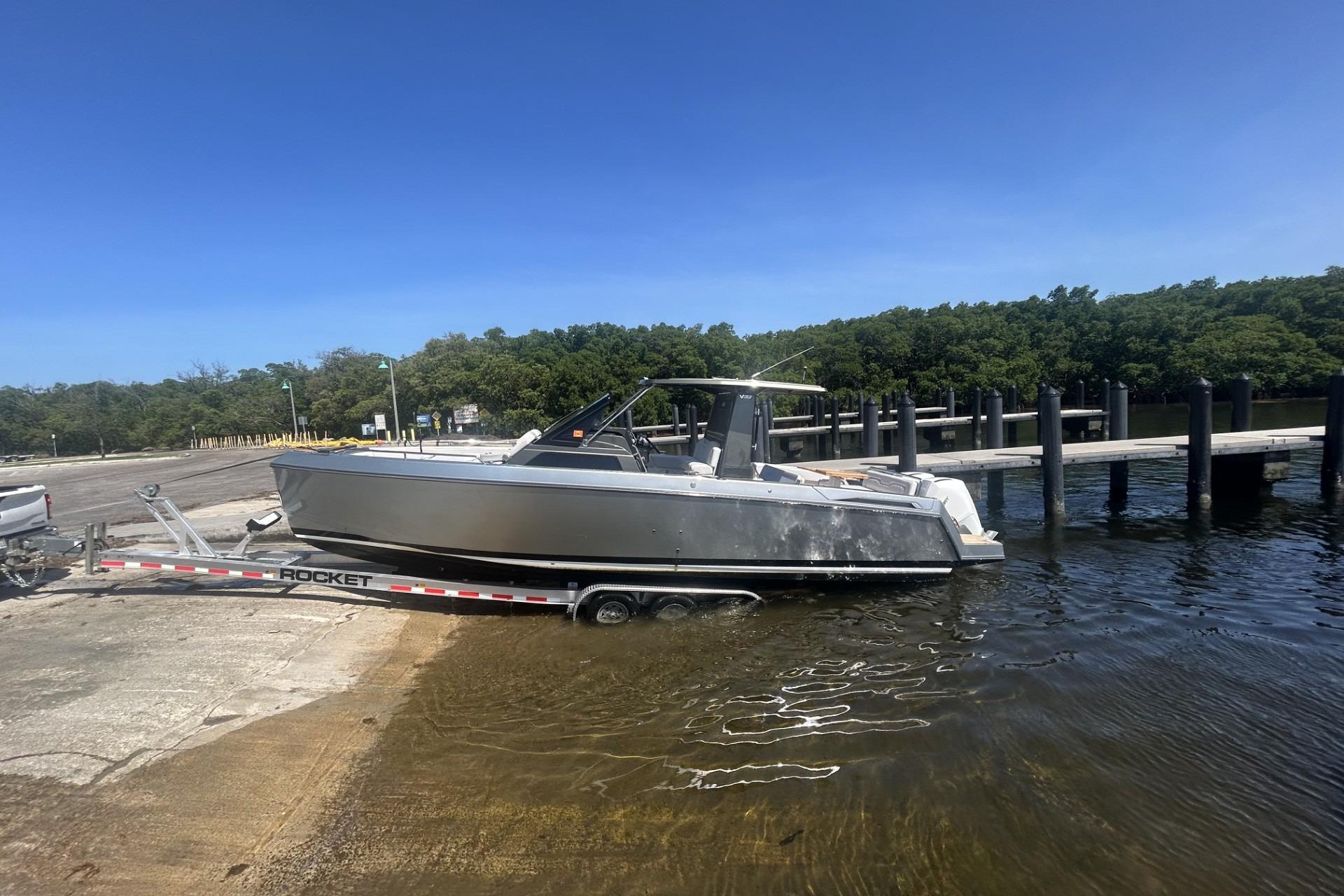 2023 Schaefer V33 boat on trailer at boat ramp, clear sky, and dock in background.