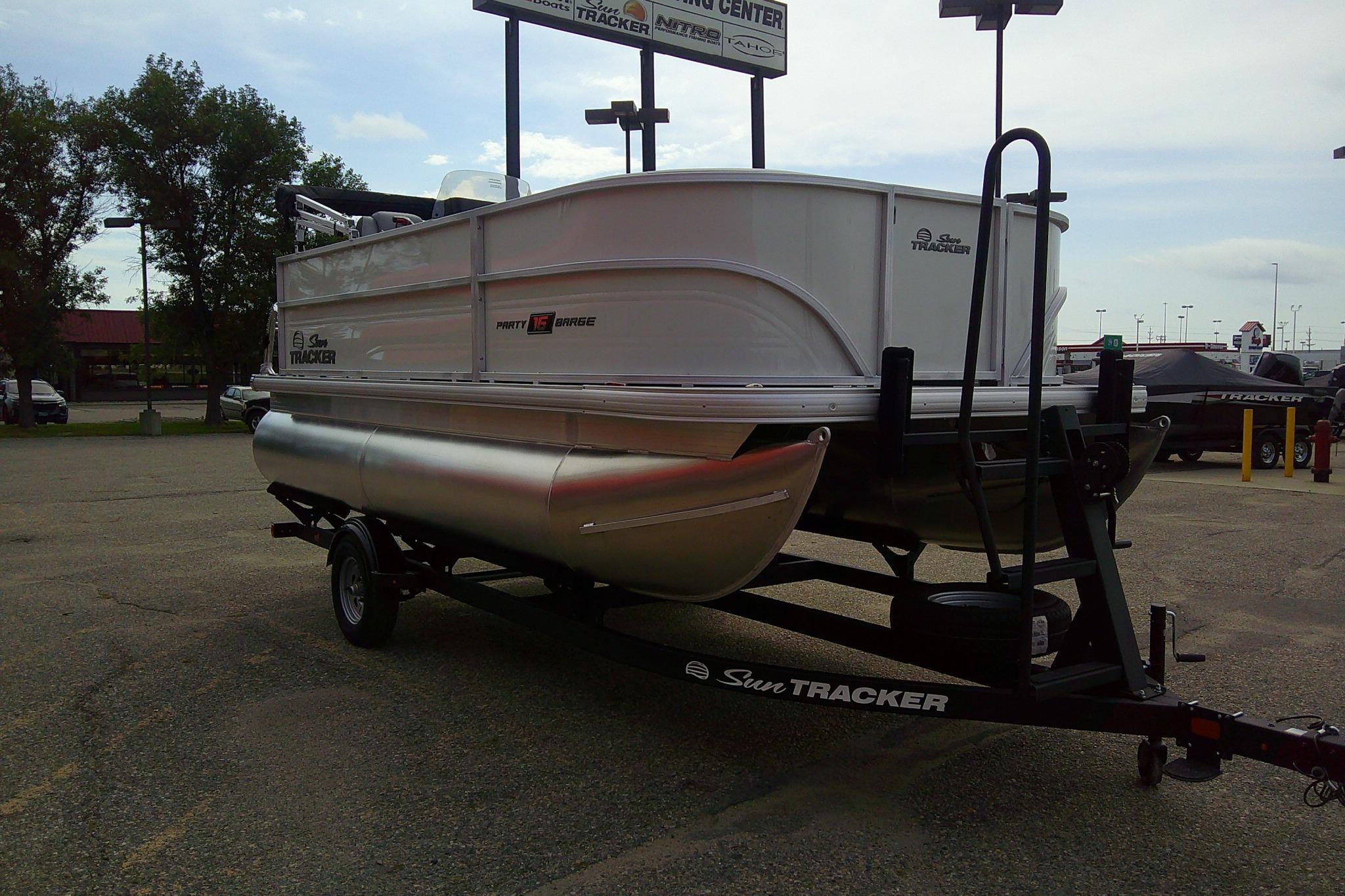 2026 Sun Tracker Party Barge 16 DLX pontoon boat on trailer in parking lot.