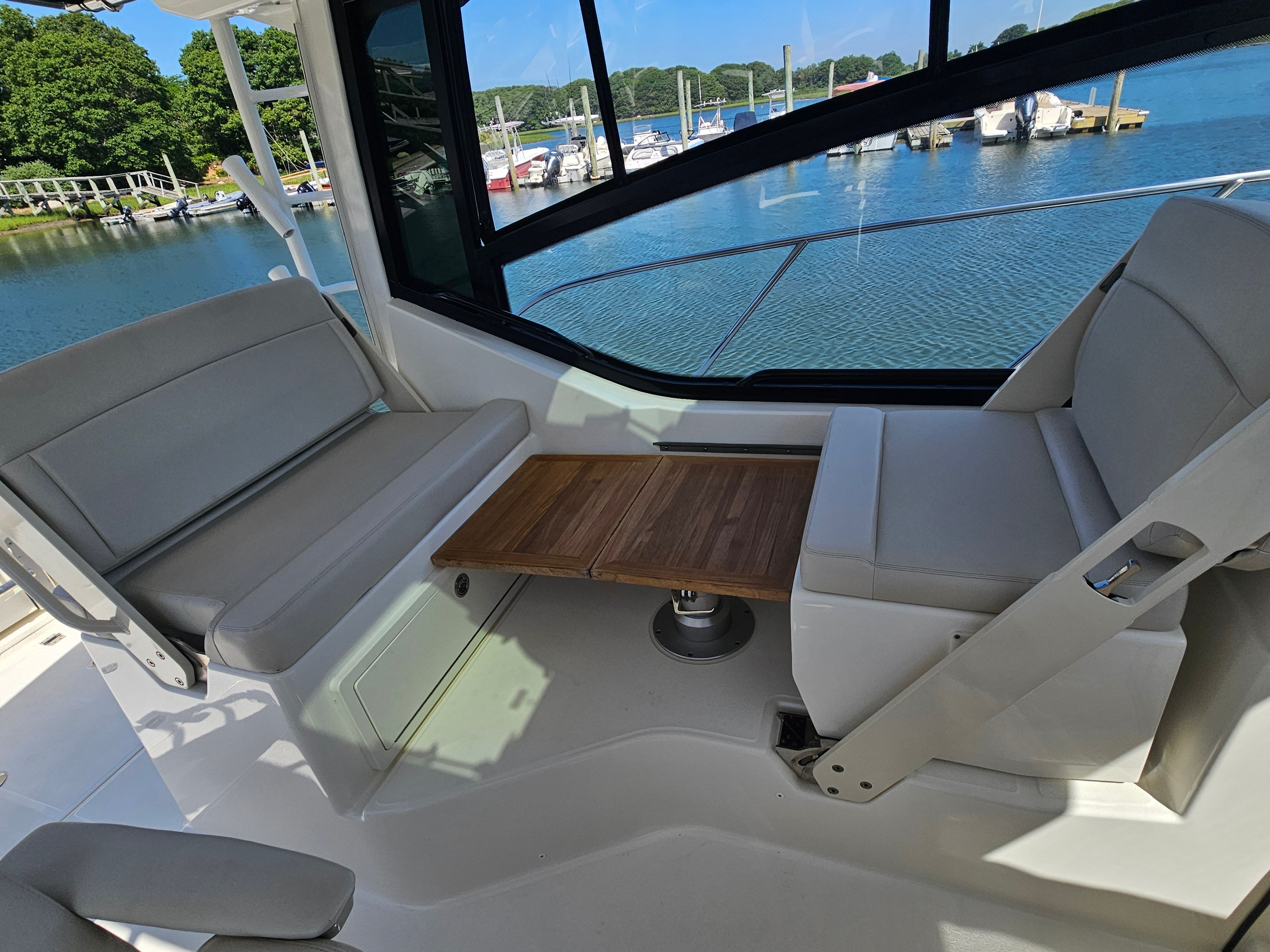 Interior of a Boston Whaler 325 Conquest with seating area and wooden table, overlooking a marina.