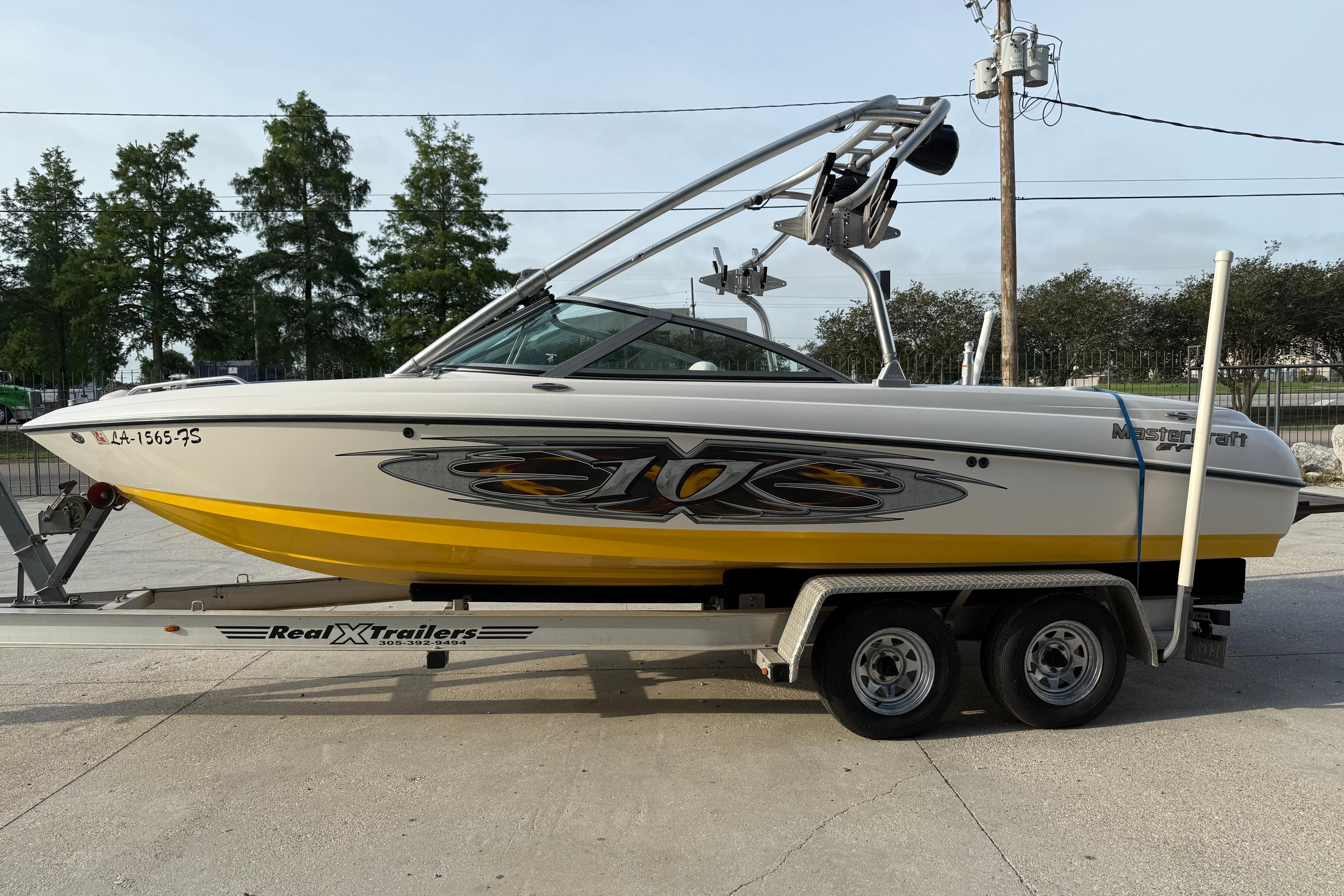 2005 MasterCraft X10 boat on trailer, yellow and white design, parked outdoors.