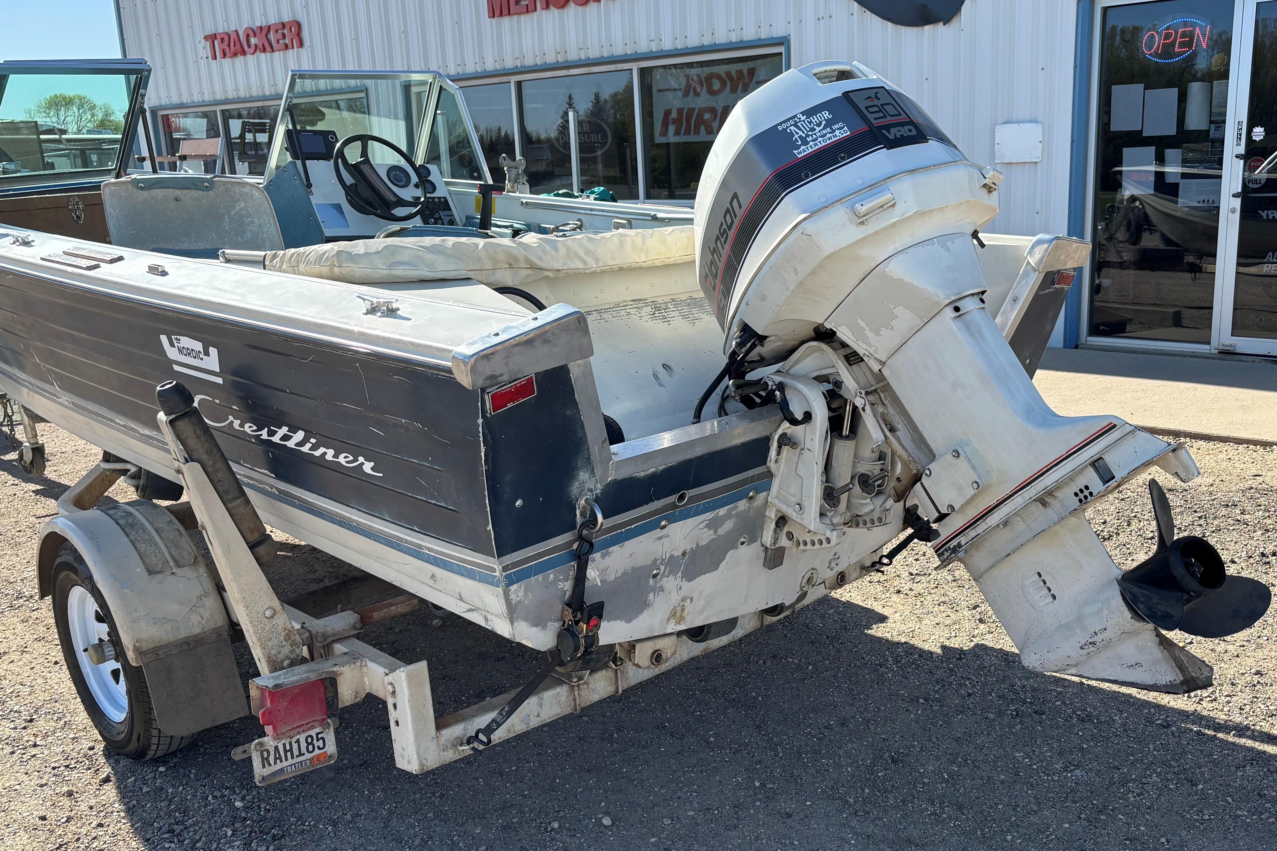 1983 Crestliner 16 boat with Johnson outboard motor on trailer, parked outside dealership.