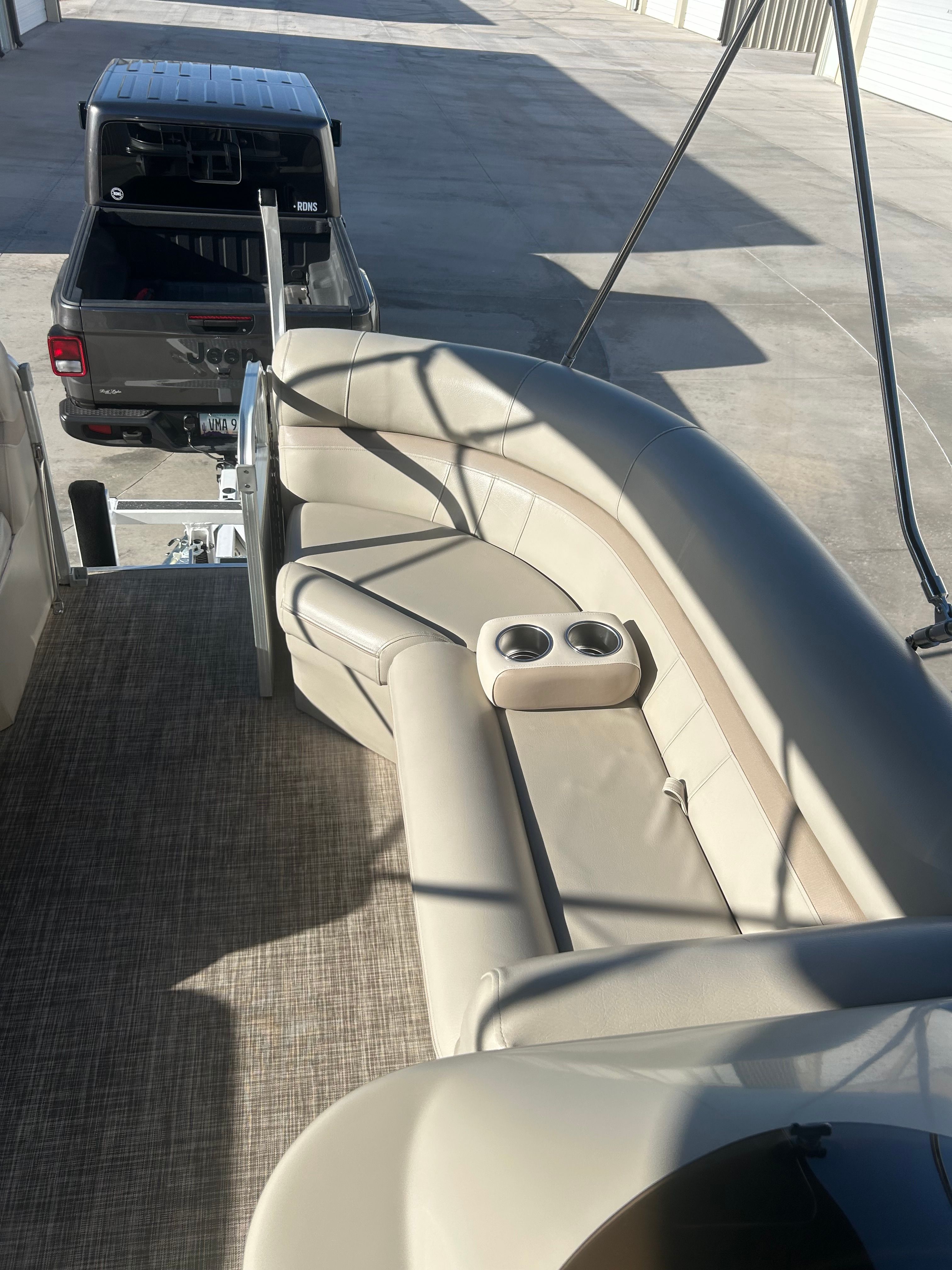 The image shows the interior of a 2018 Berkshire 24RFX CTS pontoon boat. It features beige upholstered seating with cup holders and is parked on a trailer behind a pickup truck.