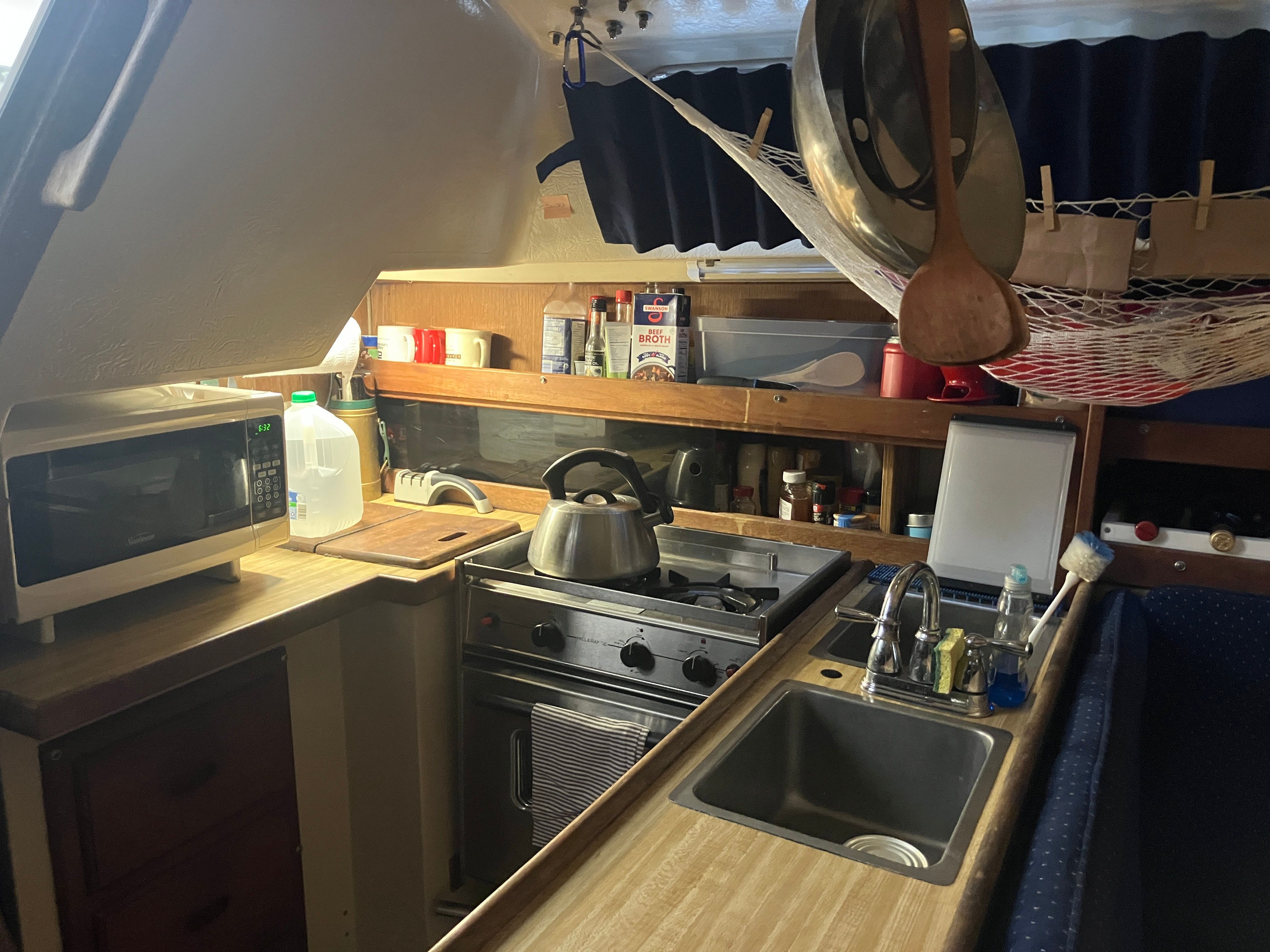 The galley of a 1984 Catalina 30 with a stove, sink, and hanging shelves.