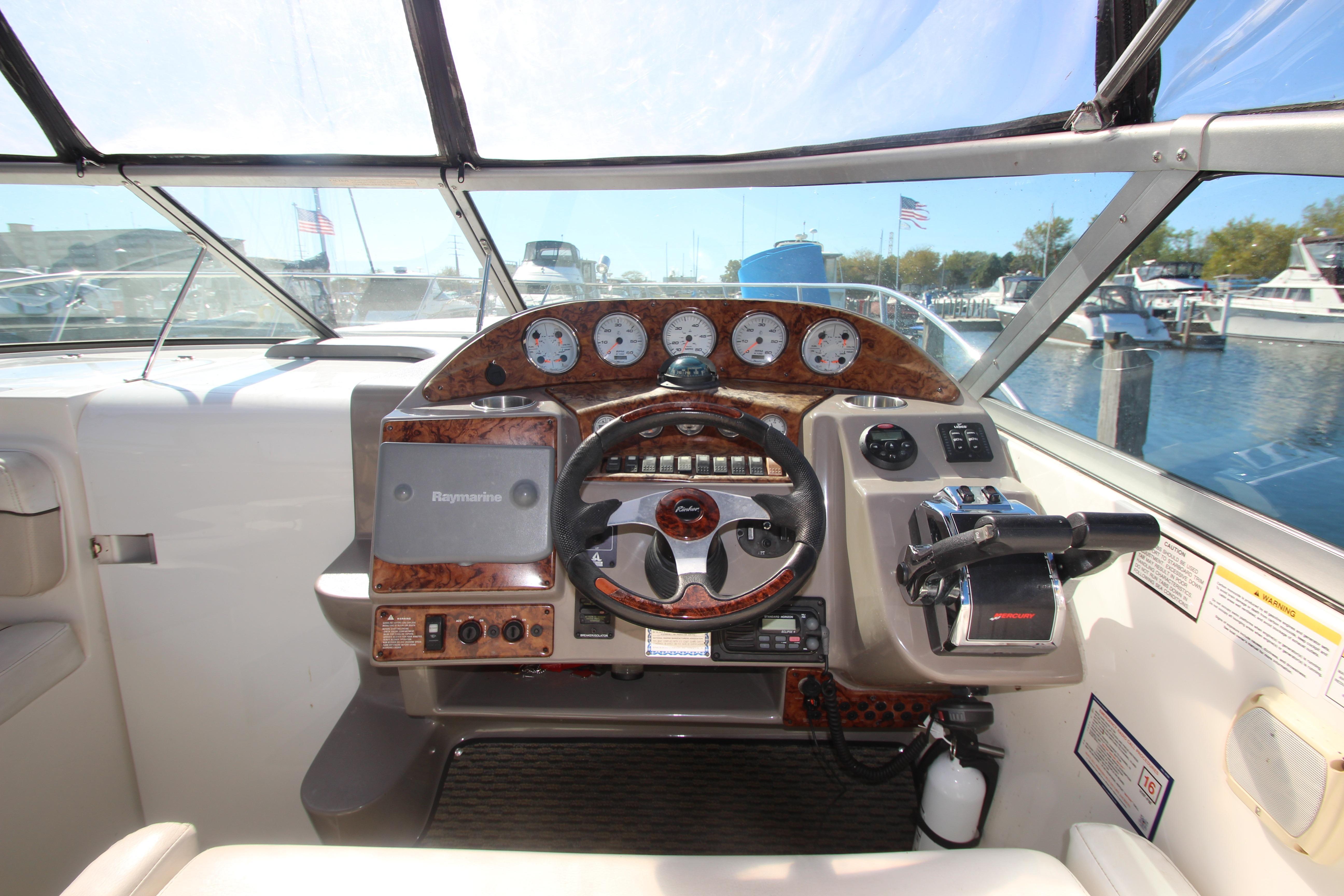 2006 Rinker 320 Express Cruiser helm with steering wheel and control panel, docked at marina.