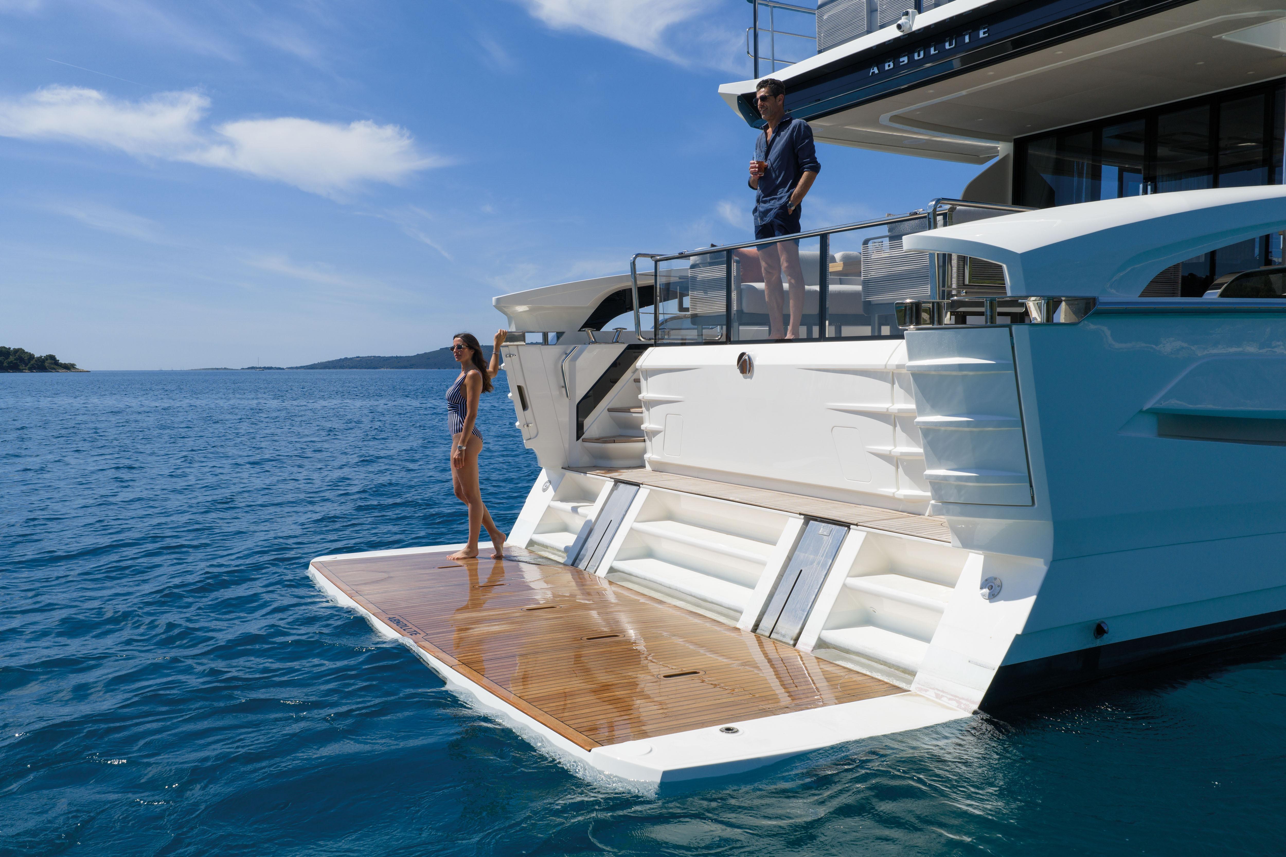 A luxury yacht with two people on deck, surrounded by blue water.
