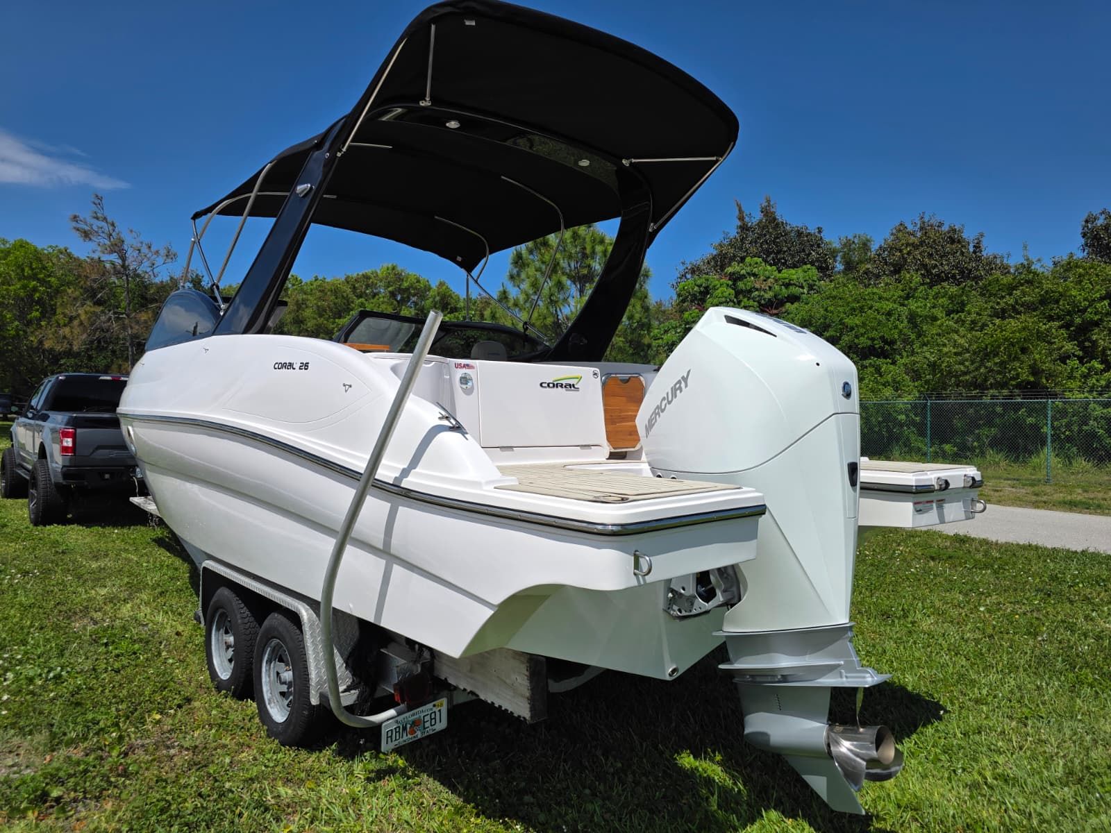 A white boat on a trailer with a black canopy and a Mercury engine.