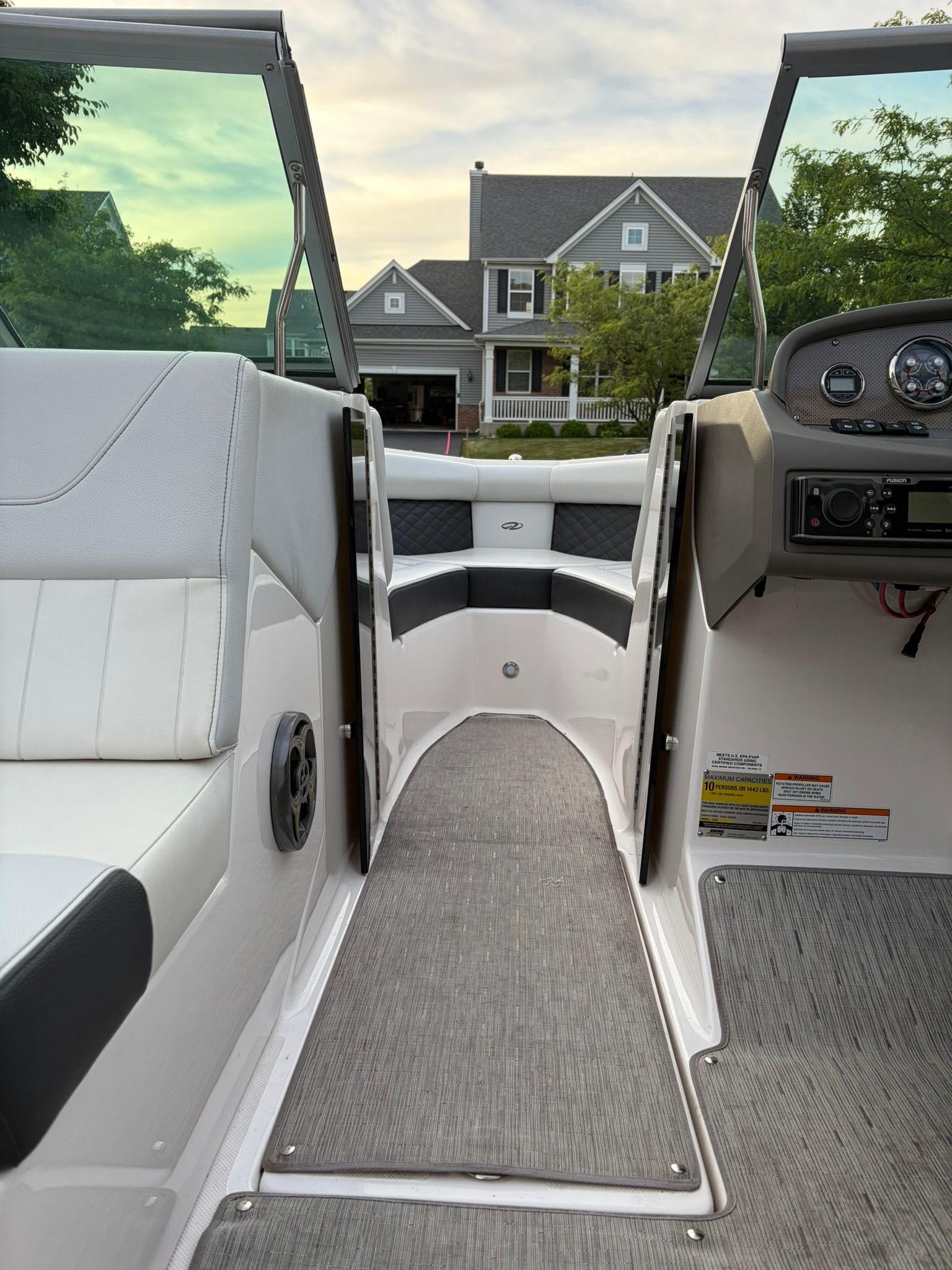 View from inside a boat with white seats and gray flooring. A house is visible in the background.