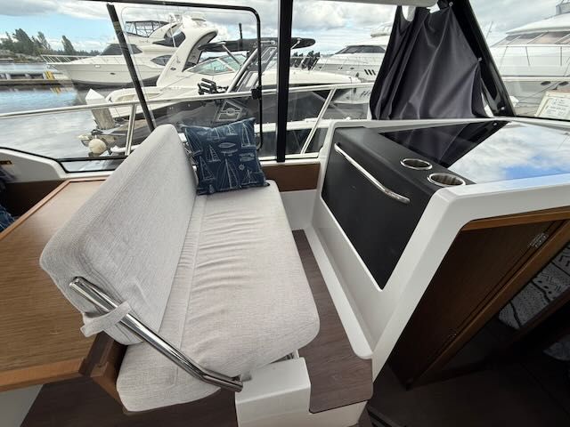 Interior of a Jeanneau NC 1095 with a bench and table, surrounded by other boats in the marina.