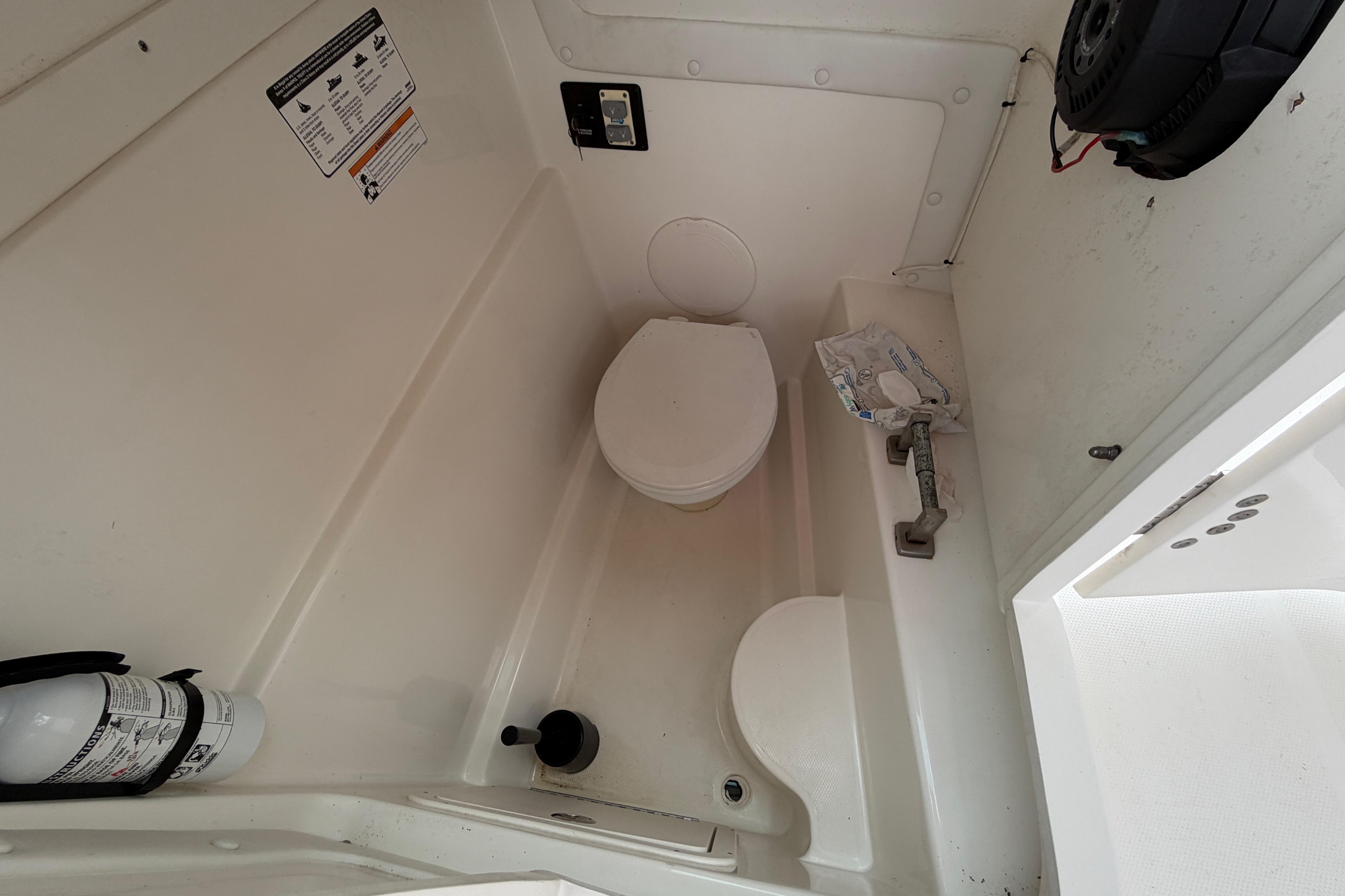 Interior of a 2019 World Cat 230 DC boat's compact bathroom with toilet and fire extinguisher.