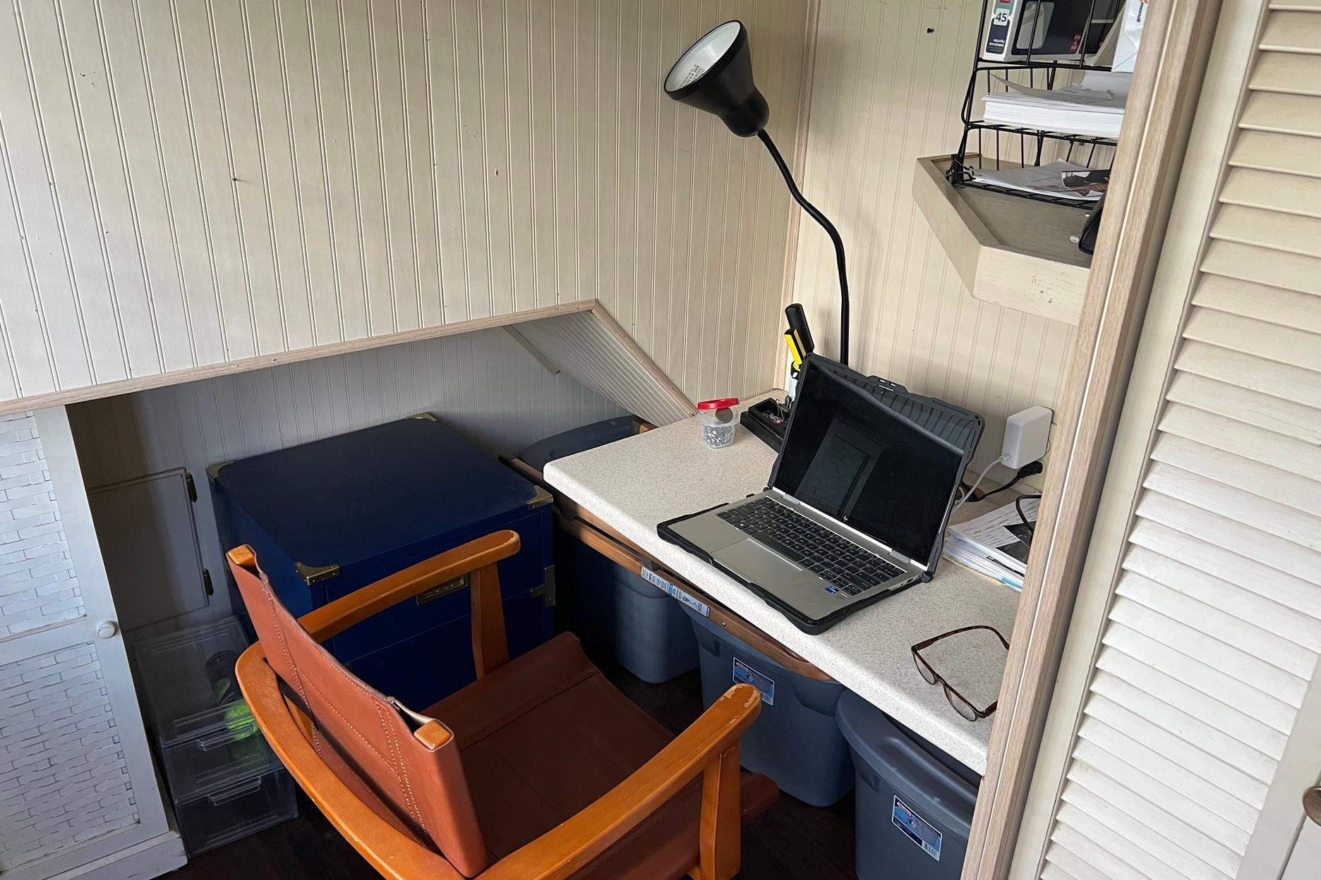 Compact workspace on a 1993 Sumerset houseboat with laptop, chair, and storage bins.