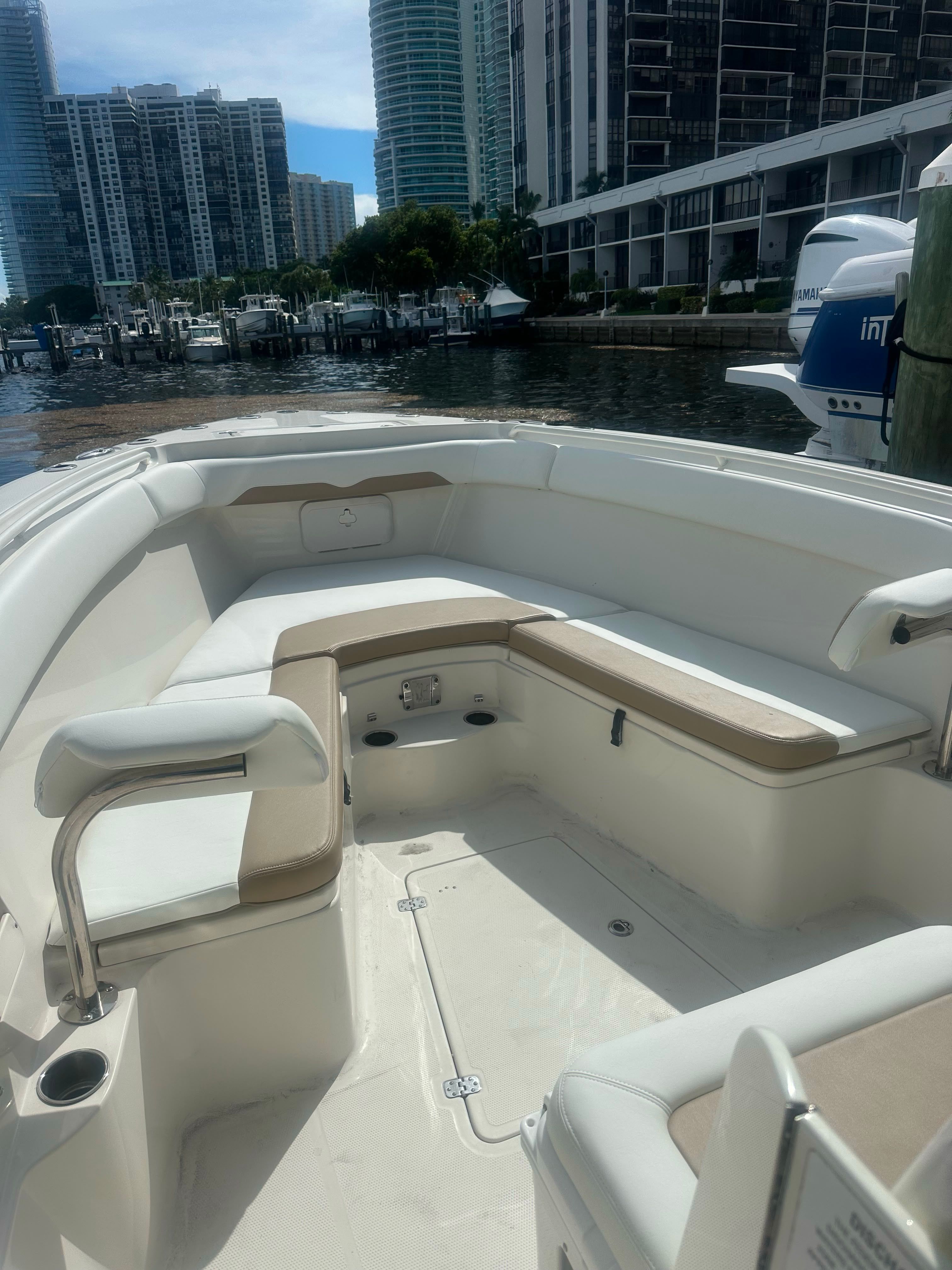 The image shows the bow of a 2017 Sailfish 320 CC with beige cushions and an urban backdrop.