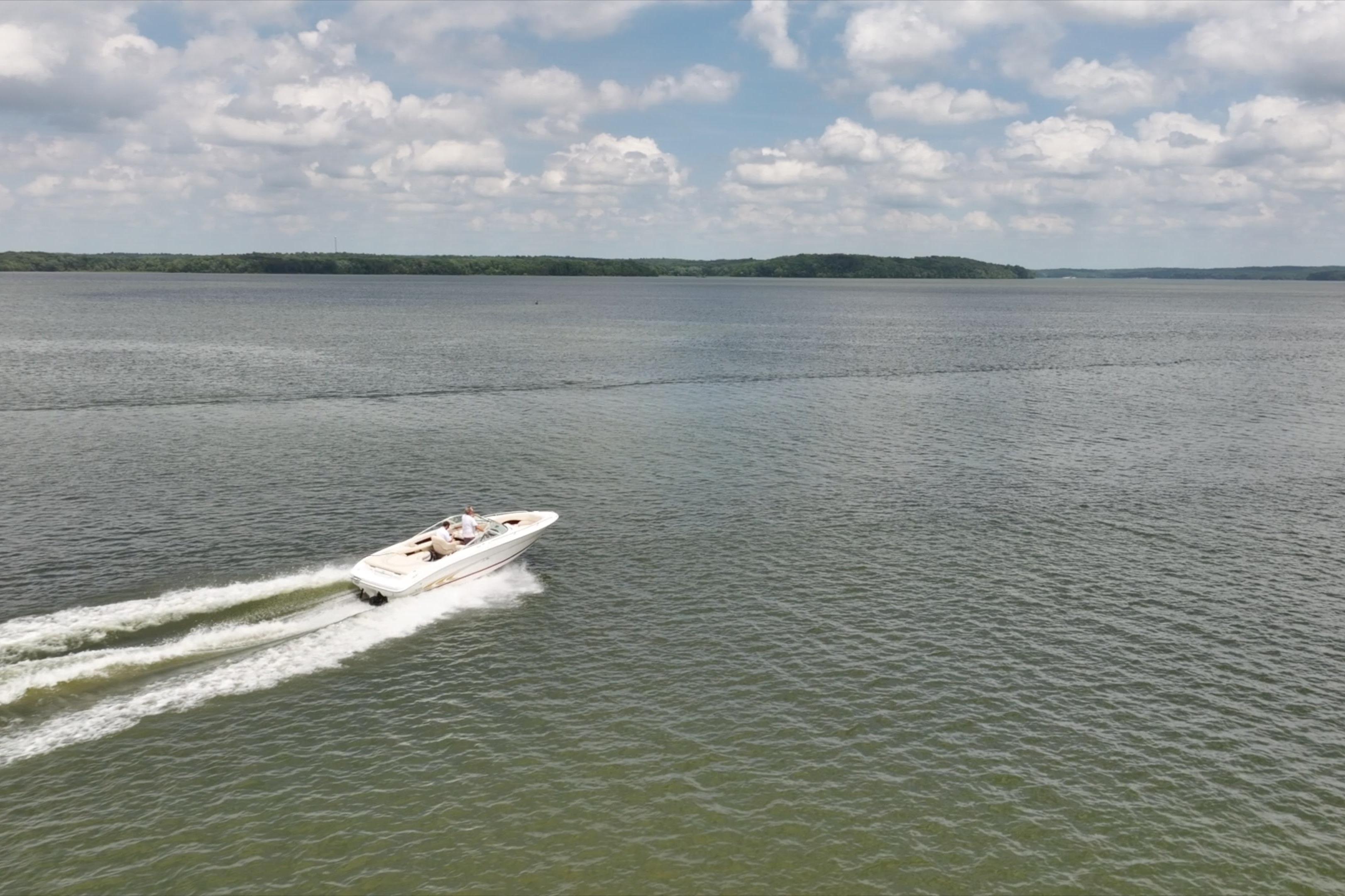 1997 Sea Ray 230 Signature boat cruising on a calm lake under a partly cloudy sky.