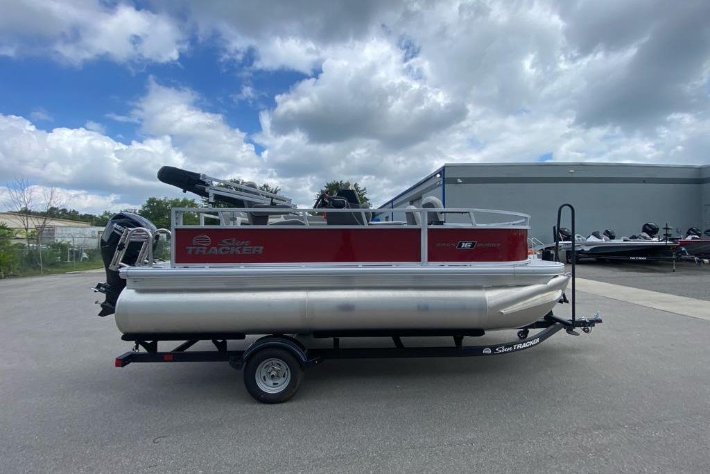 2026 Sun Tracker Bass Buggy 16 XL Select pontoon boat on trailer, parked outdoors.