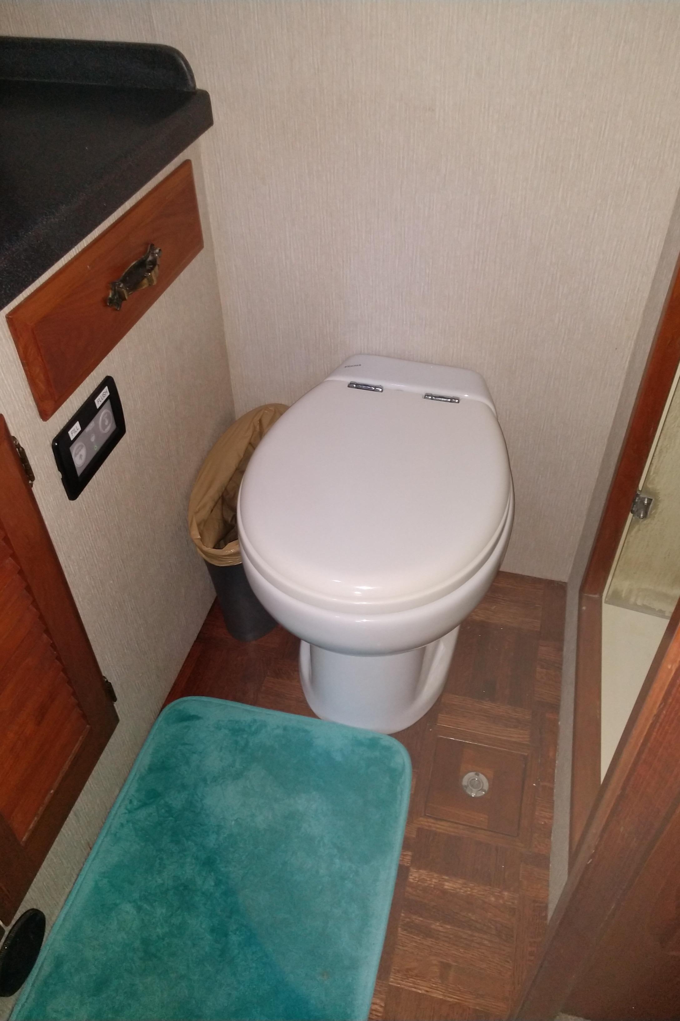 1981 Tollycraft 43 Motoryacht bathroom with toilet, teal mat, and wooden cabinetry.