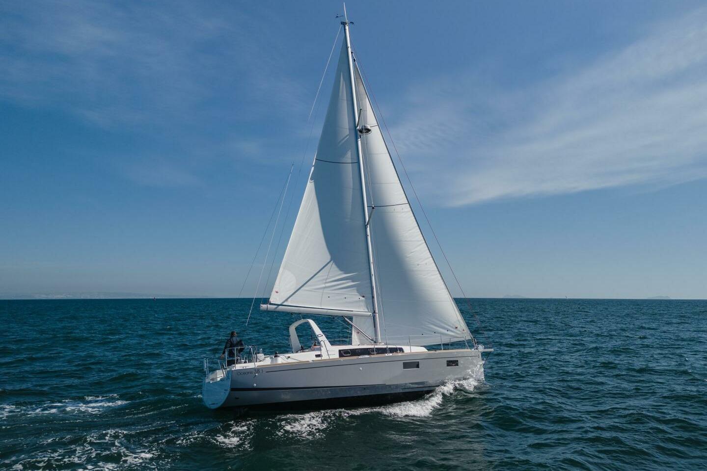 2023 Beneteau Oceanis 38.1 sailing on open sea under clear blue sky.