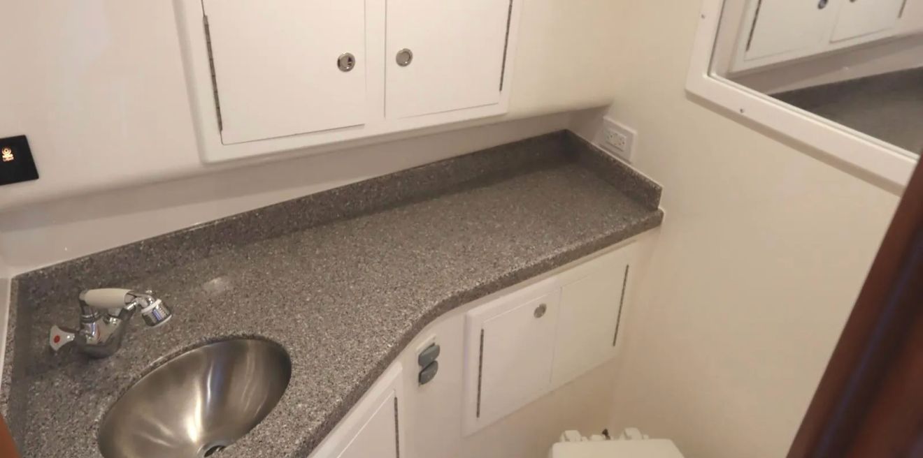 Interior view of a boat bathroom with sink, countertop, and cabinets.