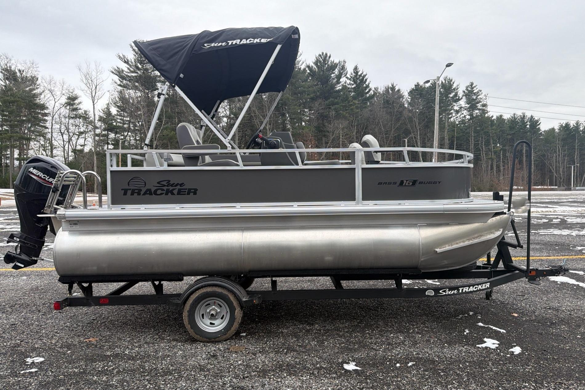 2026 Sun Tracker Bass Buggy 16 XL Select pontoon boat on trailer, parked outdoors.
